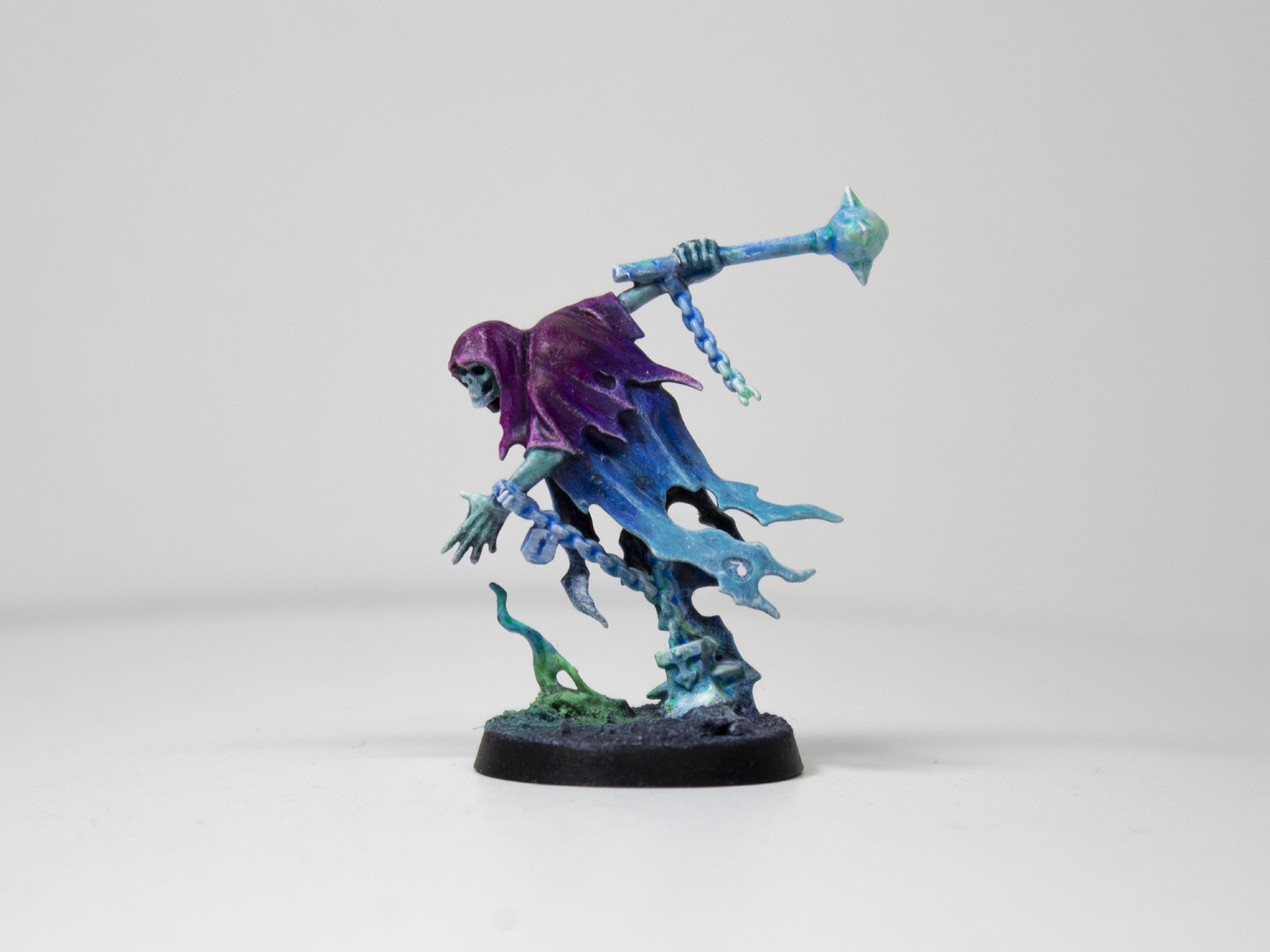 Painted miniature of a cloaked, ghastly figure lunging forward while holding a mace. It is painted in a gradient from a bright purple to a lighter blue