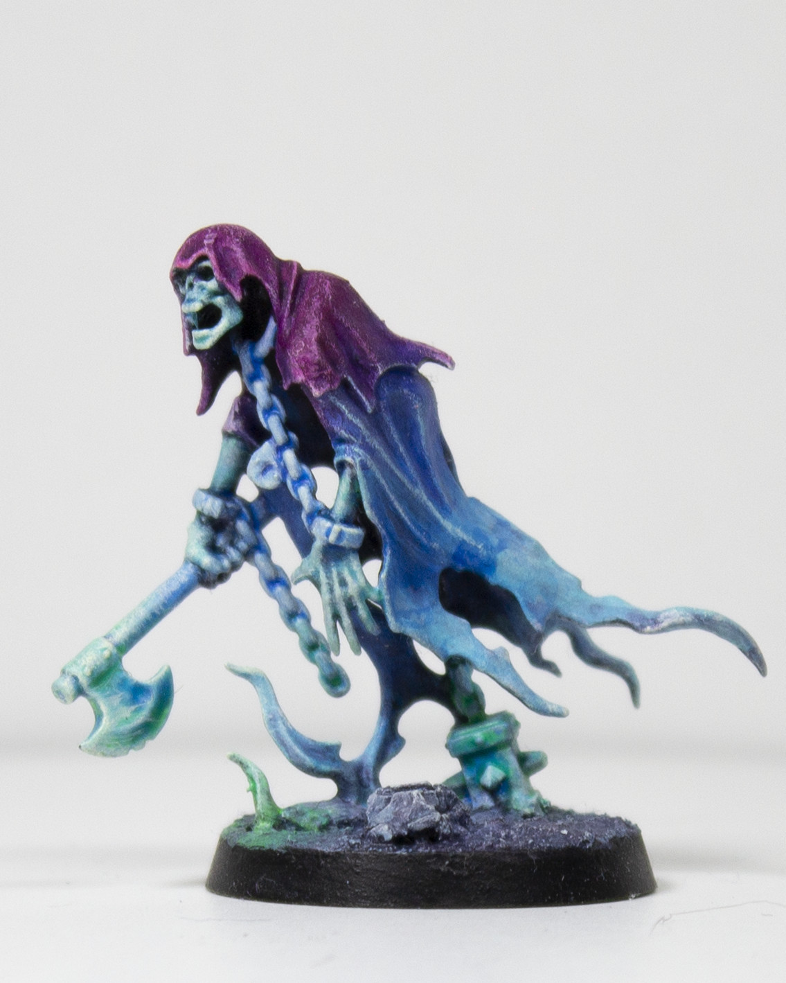 Painted miniature of a cloaked, ghastly figure holding an axe. It is painted in a gradient from a bright purple to a lighter blue, with a hint of a bright green flame emerging from the ground