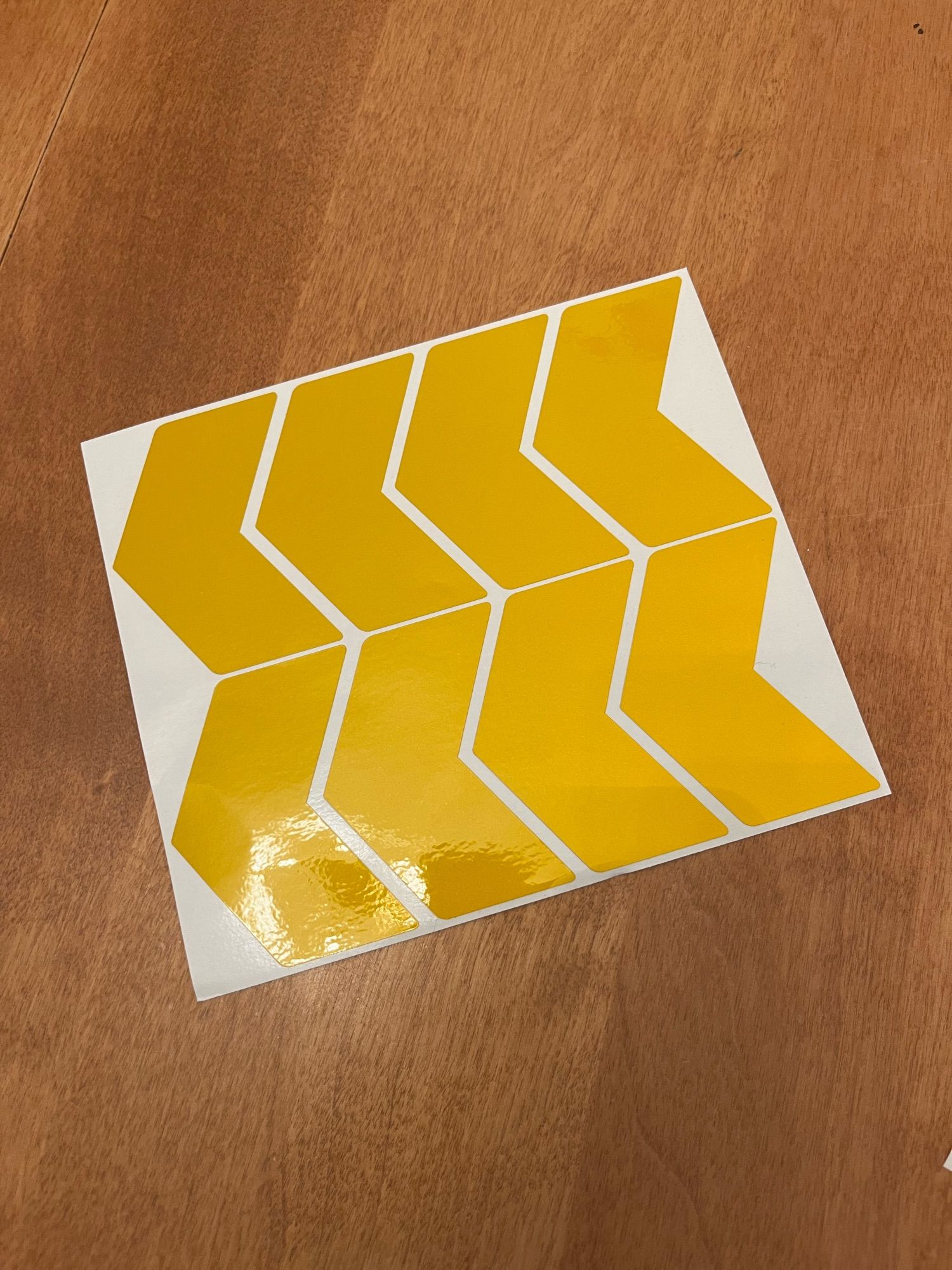 Eight yellow reflective chevron stickers on a white backing, laid on a wooden tabletop.