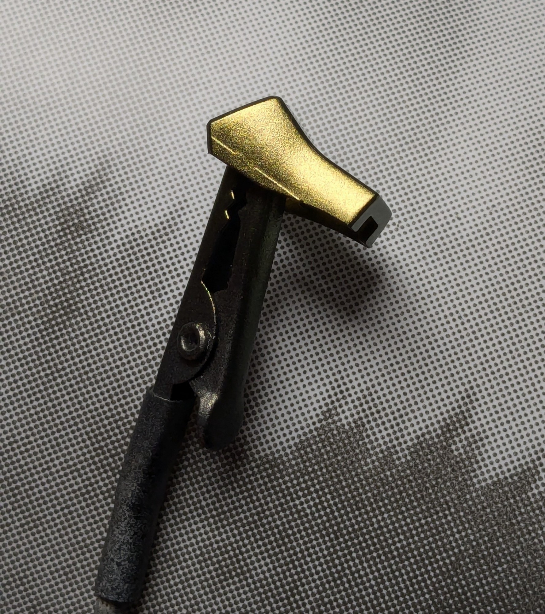 A photograph showing the side view of an art part from the high grade Hyaku-Shiki model kit. It is held in an alligator clip and is shown over a gray and dark gray background. The part, painted Topaz Gold, is reflecting a lot of light.