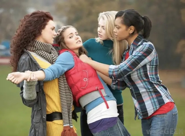 Finally, puffy vest girl gets her turn in the middle. This is definitely the most horny of all four images. Ponytail girl is holding her by the puffy vest and pushing her backwards, making her lean back into scarf girl's arms. Scarf girl has a hand wrapped around her wrist. Turquoise shirt girl appears to be gripping the top of her head. Meanwhile, puffy vest girl is staring directly into the camera with a face that seems to suggest she knows this is an inappropriate time and place for a kinky lesbian fourway but she has already accepted the inevitability that she is going to surrender to this overwhelming arousal and that after some scuffling and negotiation its been firmly established that she is going to be on bottom for all three girls. She doesn't look particularly unhappy about this. In my opinion.