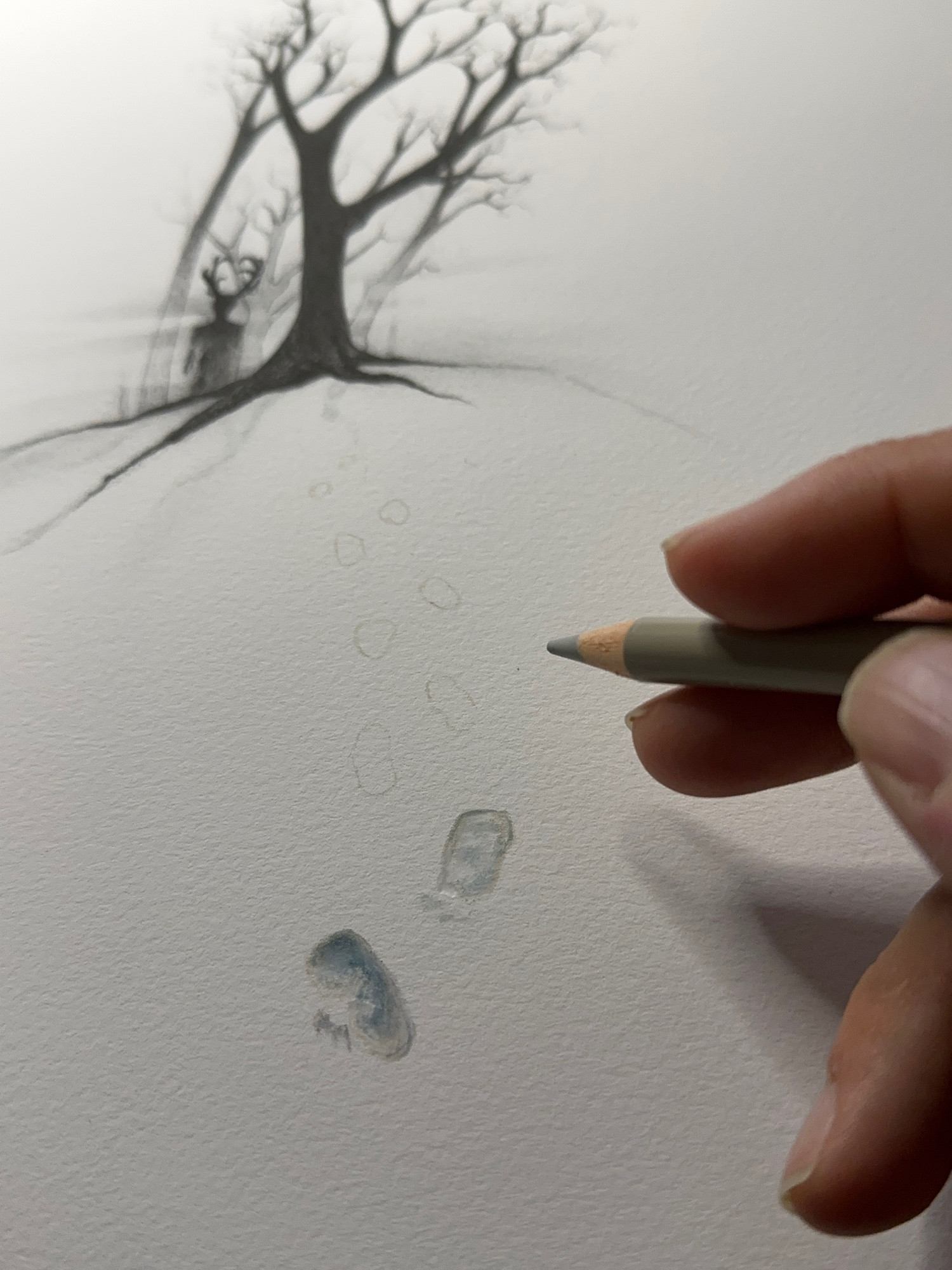 Hand holding a colored pencil over a print where two footprints in the snow appear. The faint outline of more footprints to be drawn leads to a Wendigo in the trees.