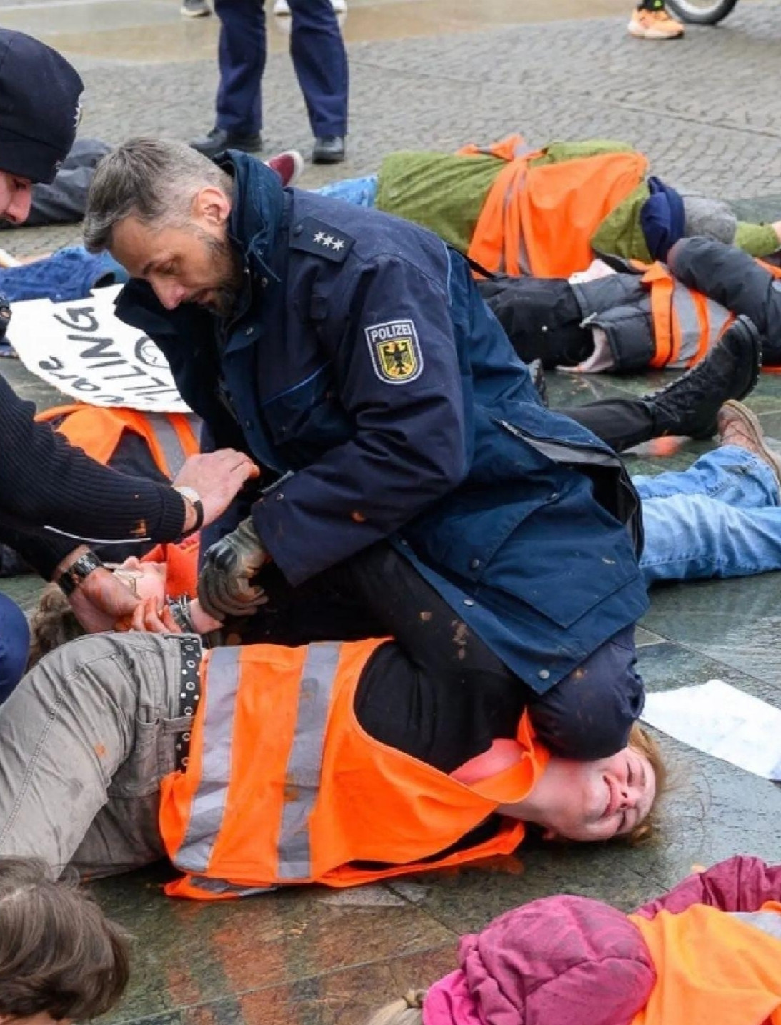 Ein Polizist kniet auf dem Gesicht einer jugendlichen Klimaaktivistin, während er ihr Handschellen anlegt.