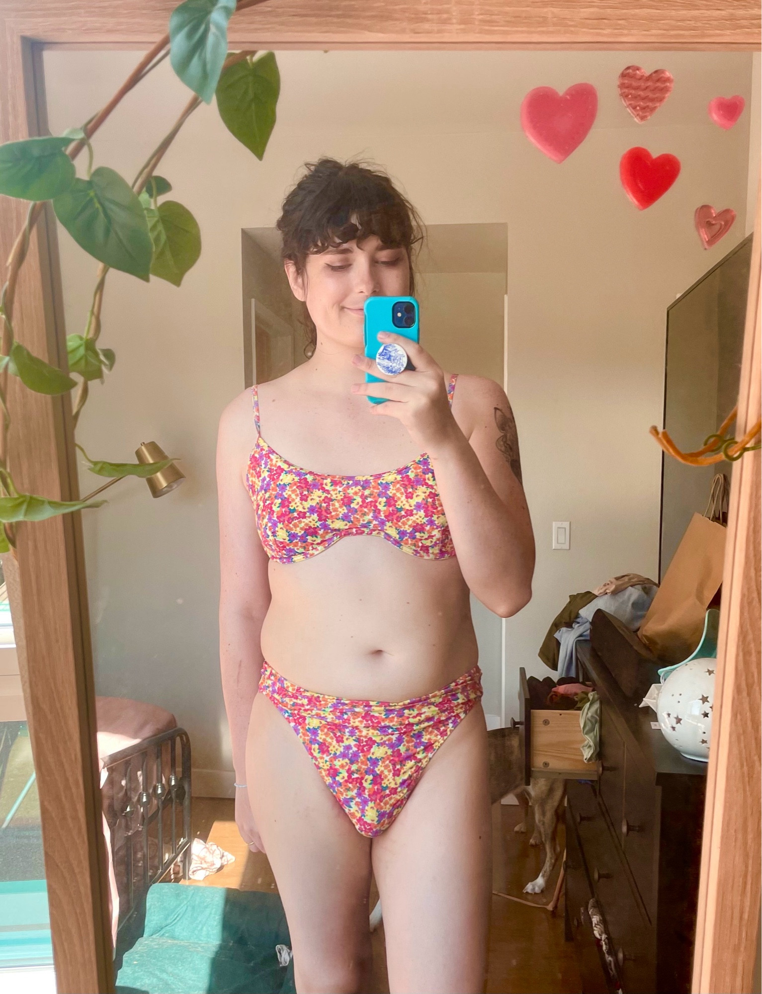 Moonreed wearing a pink, yellow, orange and violet flower print bikini, her hair is up in a ponytail