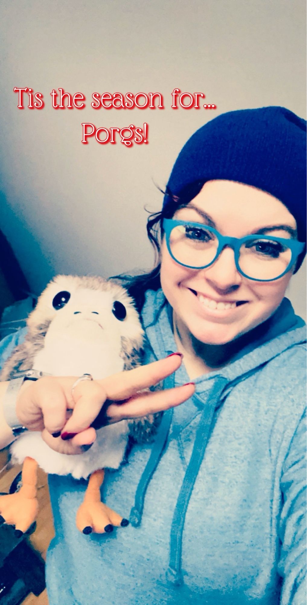 Anna, wearing a blue beanie and blue glasses holding a toy and flashing a peace sign