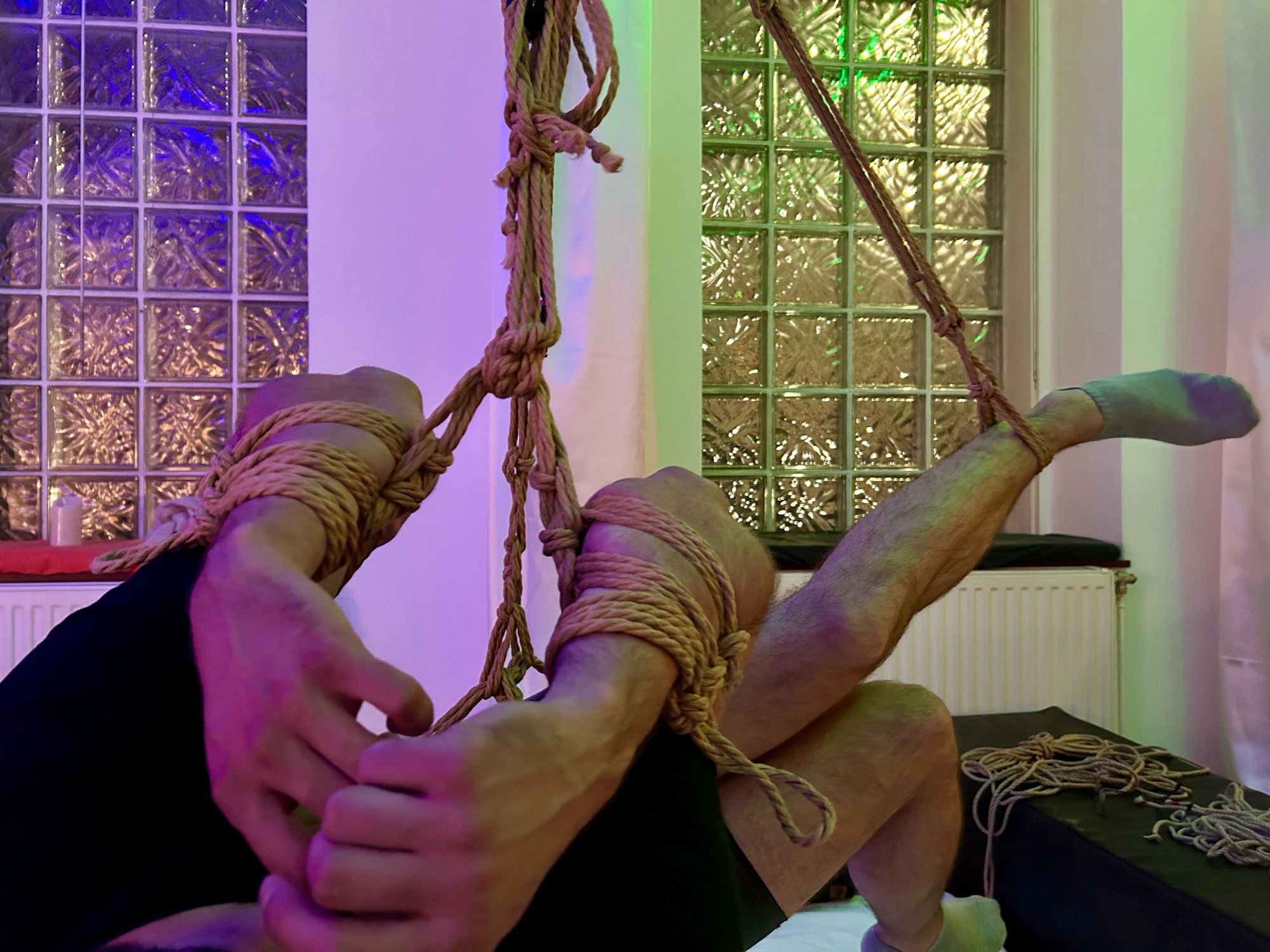 a male person being suspended in the air with jute rope, shibari style