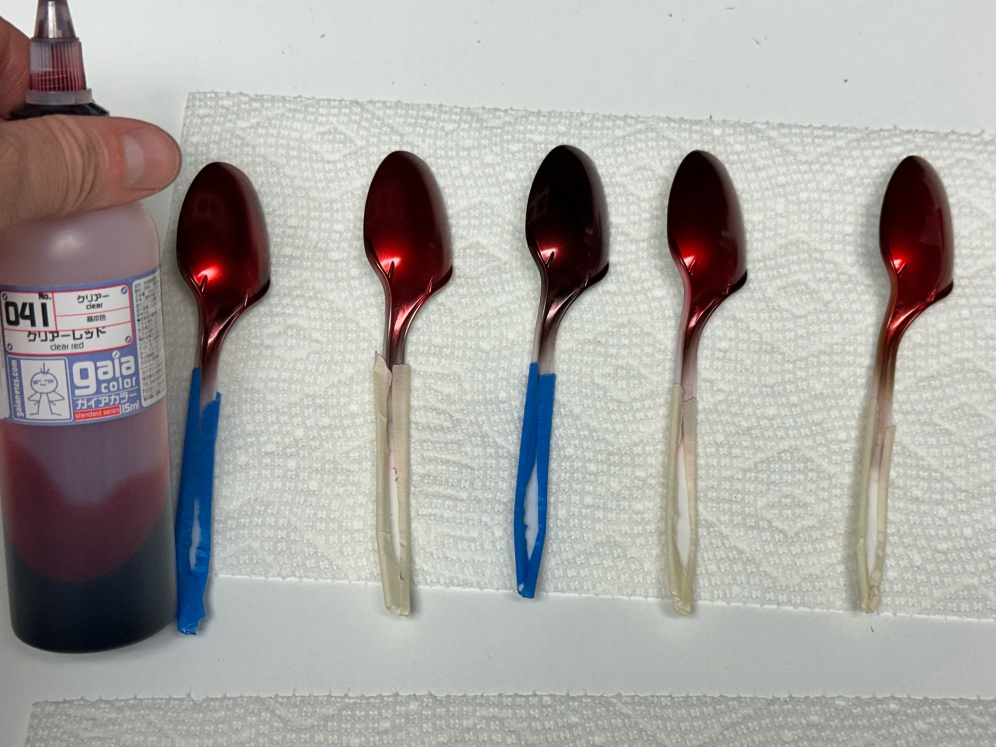 Five plastic spoons sprayed with GaiaNotes Clear Red, all over different base colors