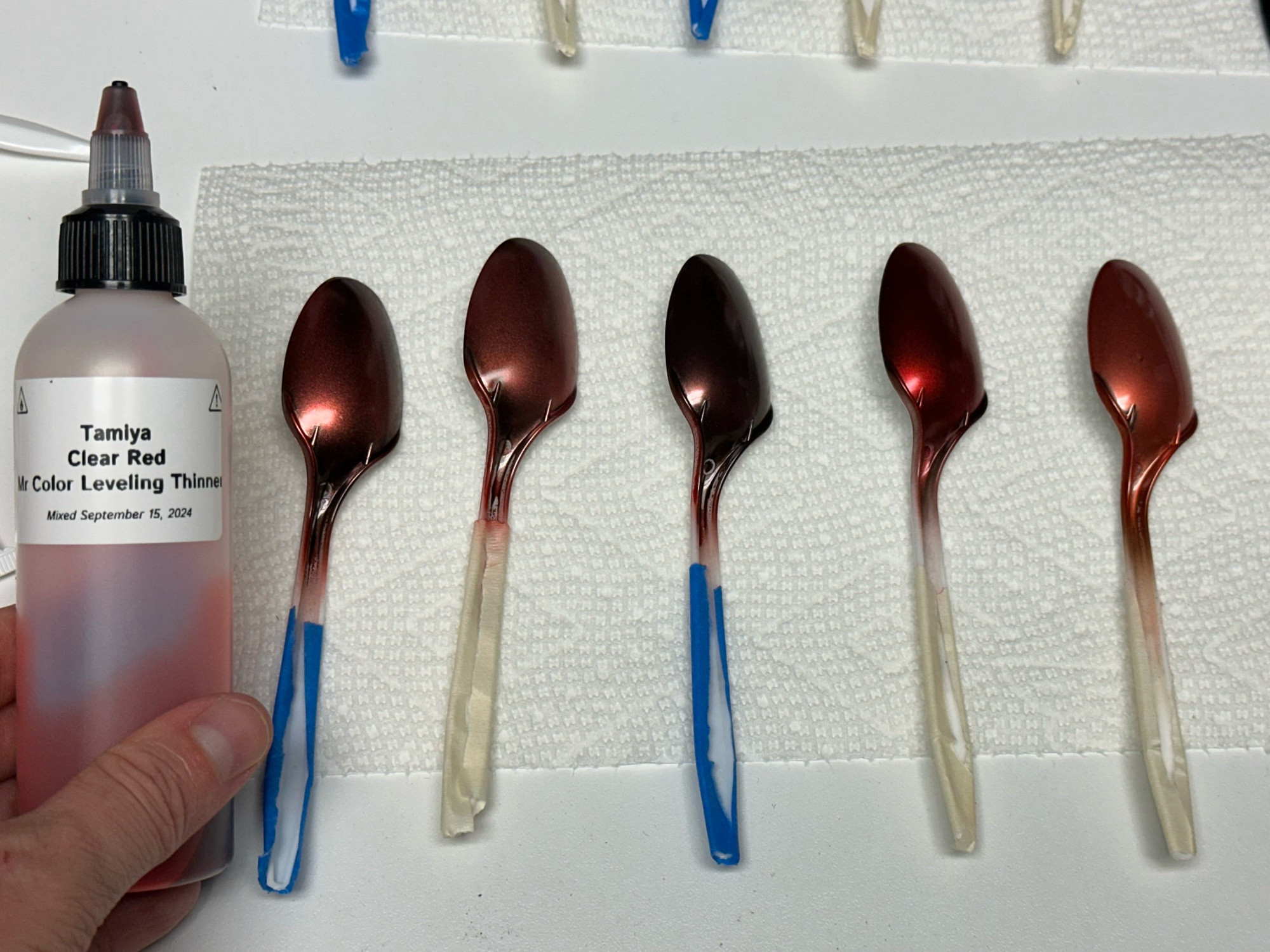 Five airbrushed spoons sprayed with Tamiya Clear Red over various base coats