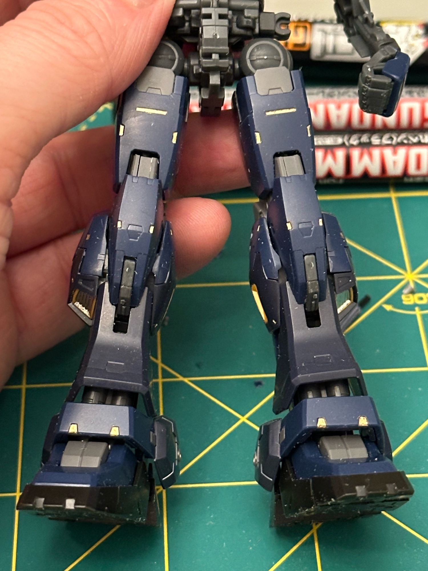 A photo of both of real grade Gundam Mk-II’s armed legs, decorated with metallic gold and chrome panel lining markers