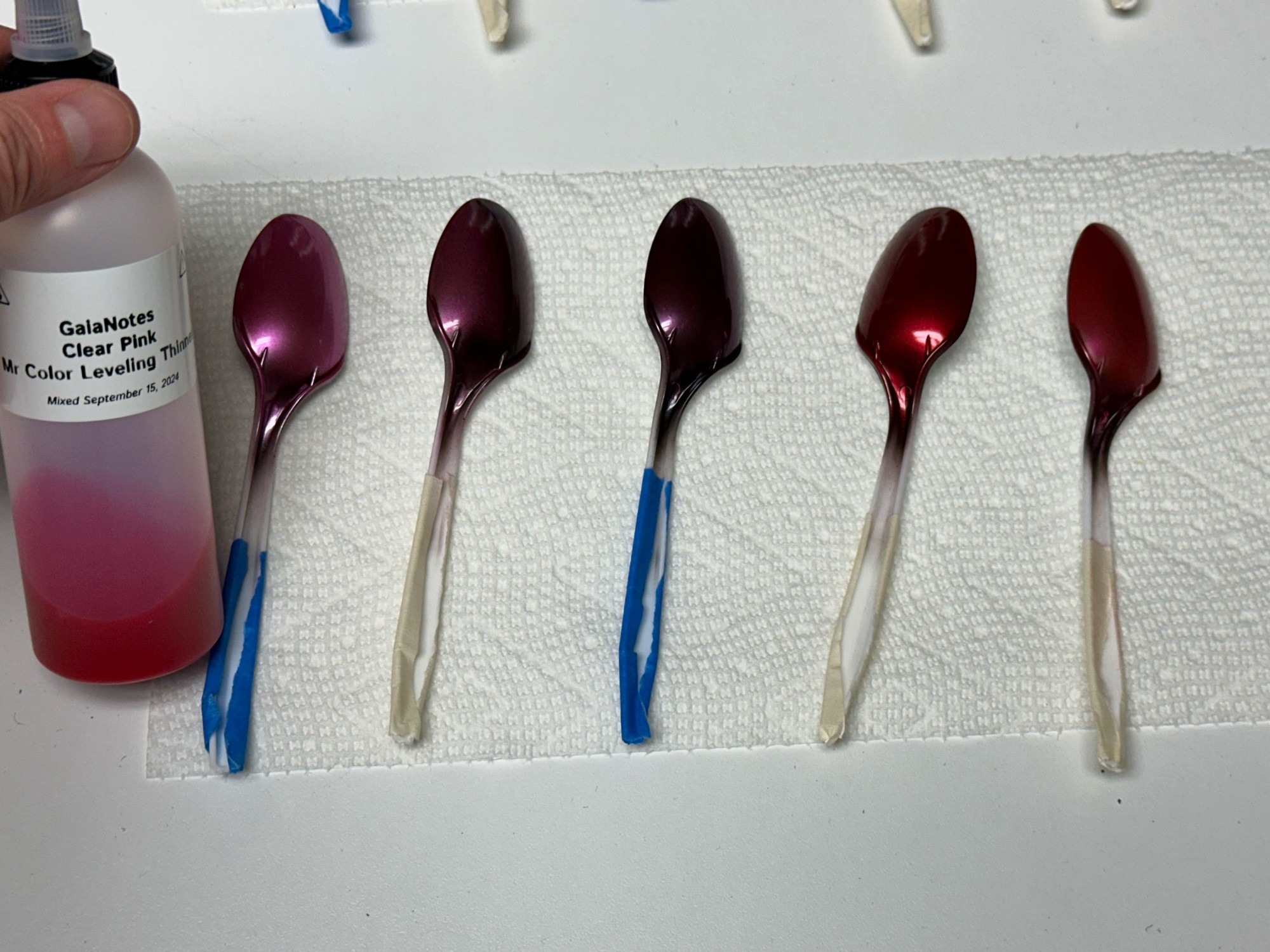 Five airbrushed plastic spoons sprayed with GaiaNotes Clear Pink over various base colors