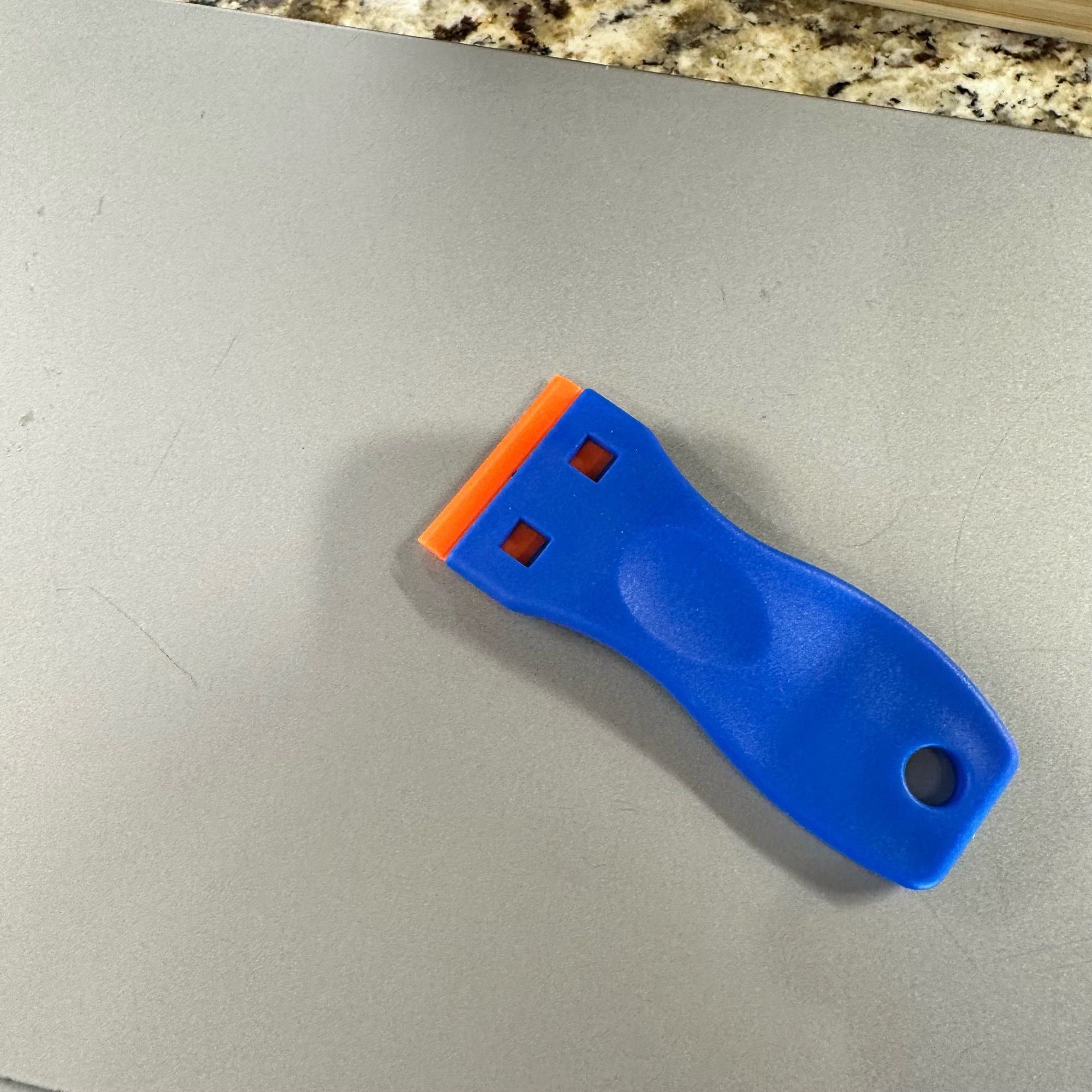 A blue plastic razor scraper