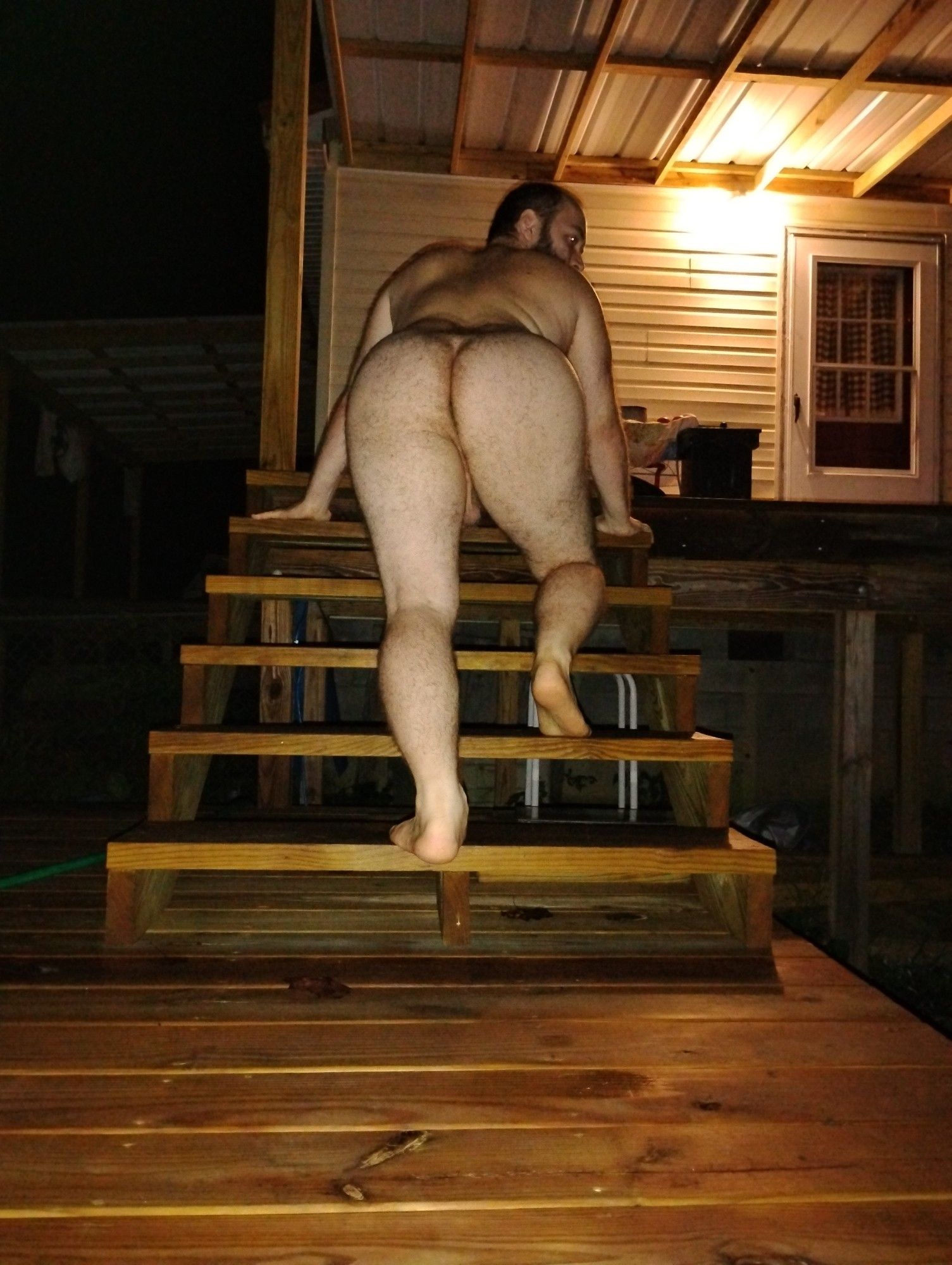 A naked hairy man (me) posing on a set of patio porch stairs.