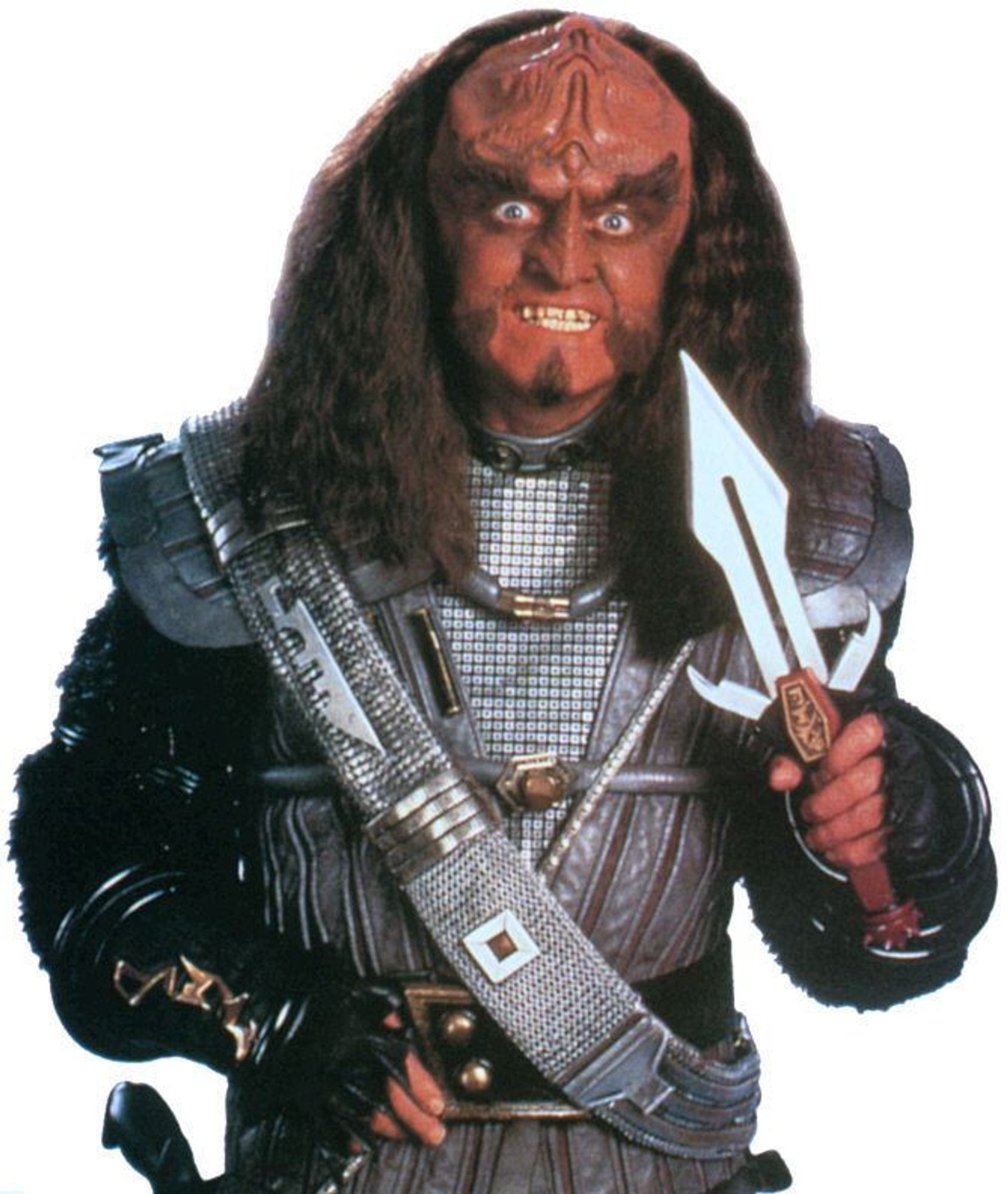 It's Gowron, from Star Trek TNG/DS9. He's got his Klingon space clothes on and a sash, a wild look and a toothy grin on his face, and holding a Klingon ceremonial dagger in his hand. He looks very intense.