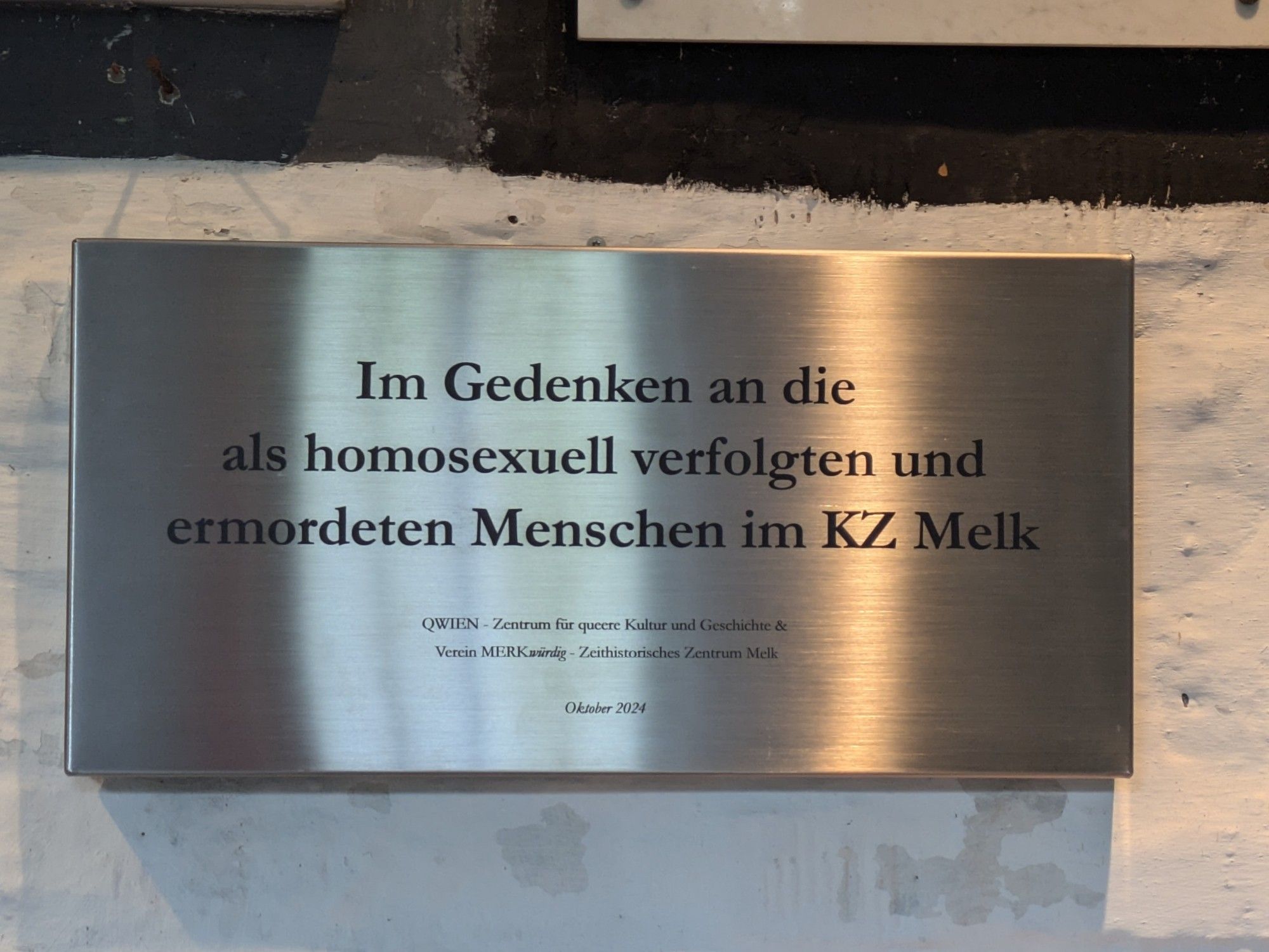 Gedenktafel aus gebürstetem Stahl (vermutlich), Text: Im Gedenken an die als homosexuell verfolgten und ermordeten Menschen im KZ Melk. Gestiftet von QWien - Zentrum für Queere Kultur und Geschichte + Verein MERKwürdig - Zeit historisches Zentrum Melk