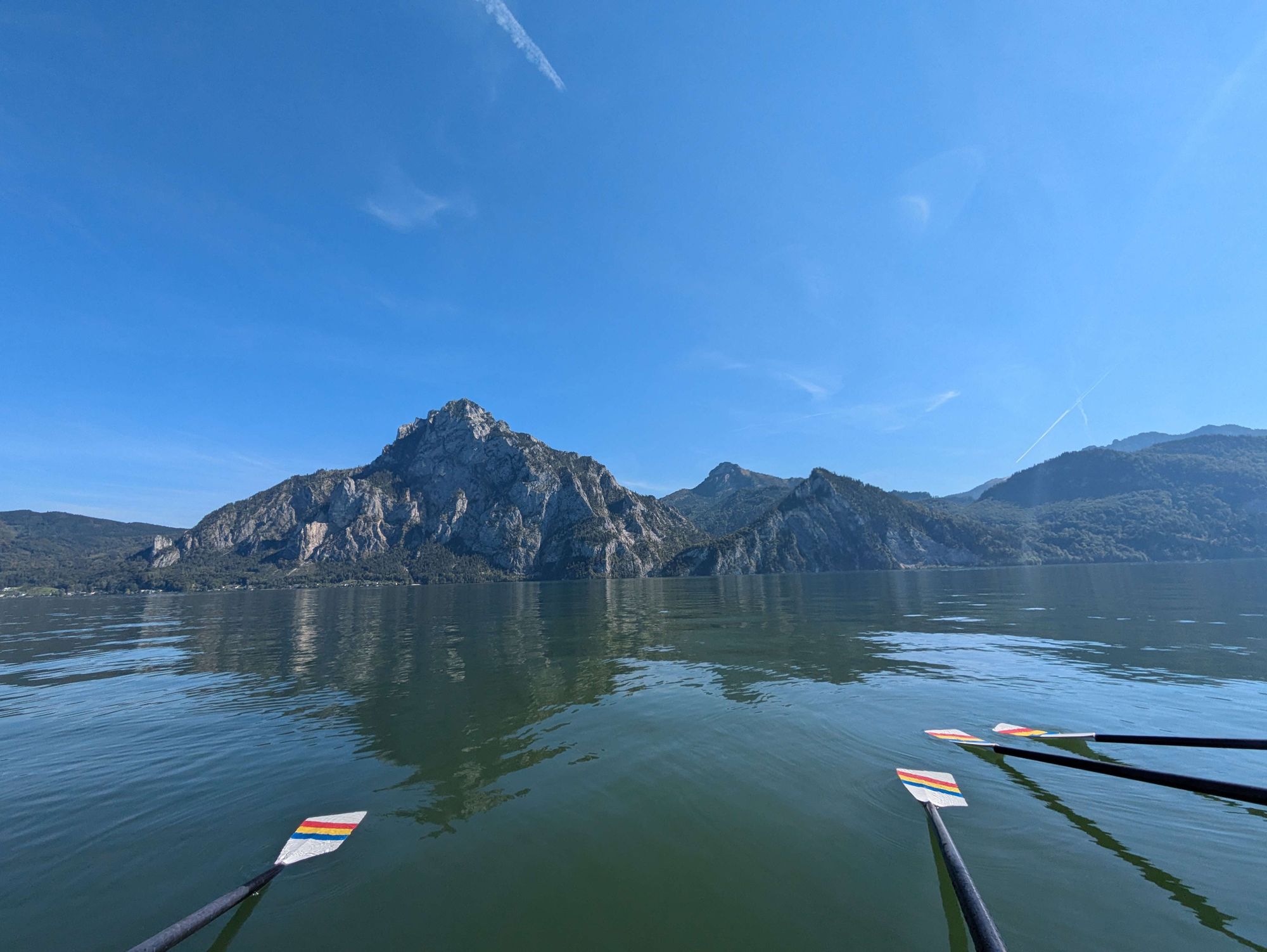 Ein Foto von einem See, begrenzt von Bergen, einer der Berge ist der Traunstein. Auf dem See sind außerdem Ruderblätter zu sehen.