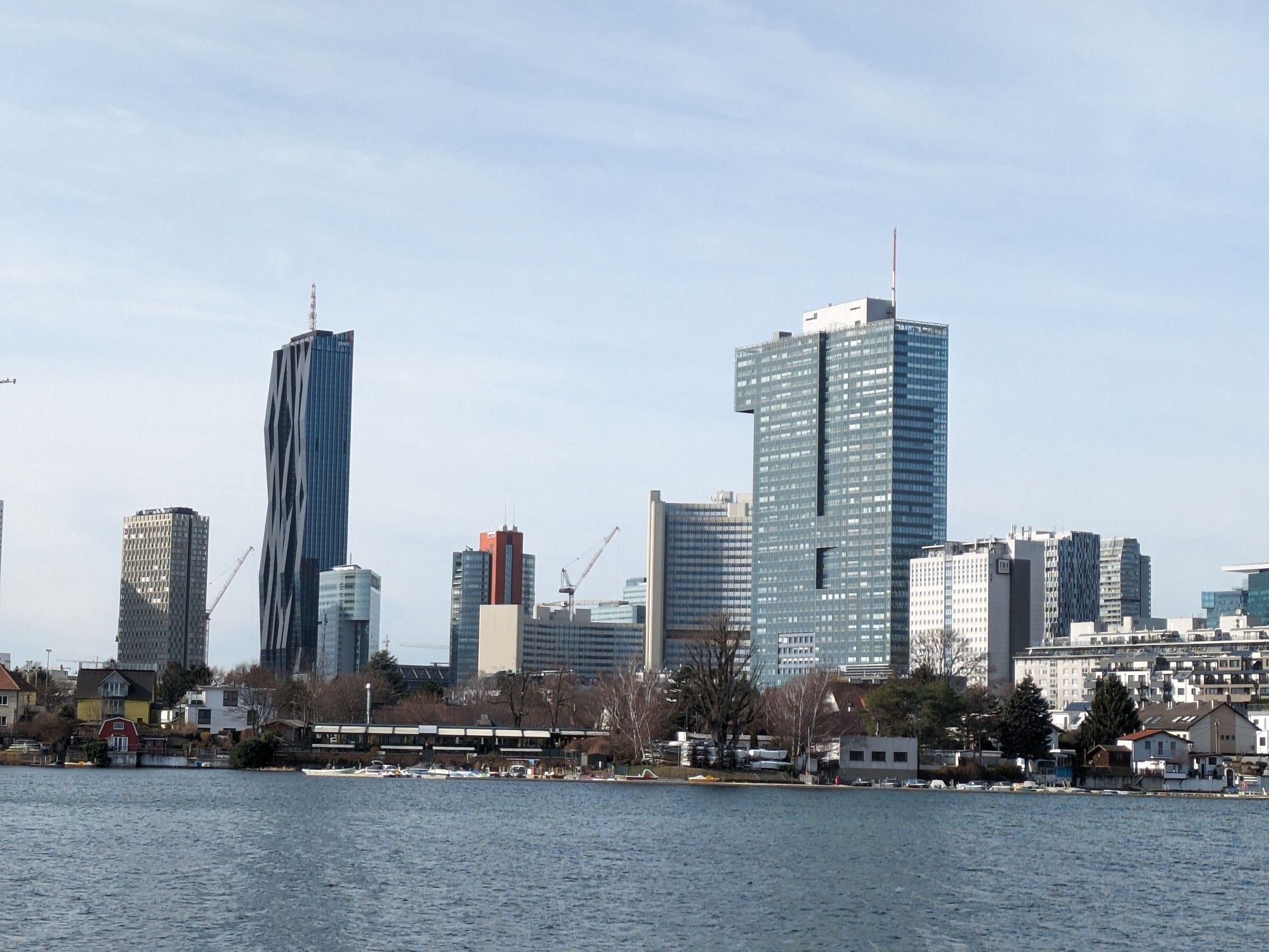 Leicht bewegtes Wasser, die Alte Donau, im Hintergrund Hochhäuser und kleine Häuser, hellblauer, leicht bedeckter Himmel