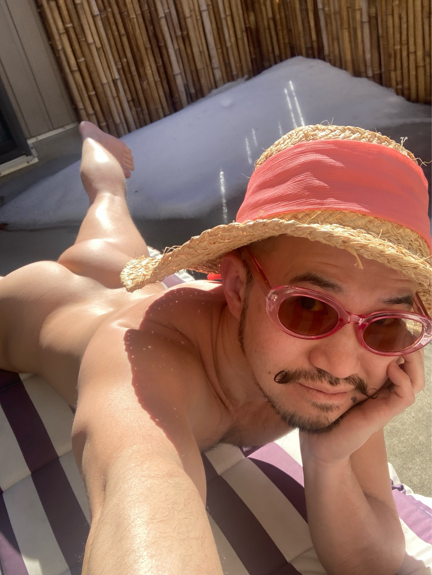 Sunbathing with a pink hat on a lounge chair on an enclosed deck with snow under the bamboo privacy fencing.