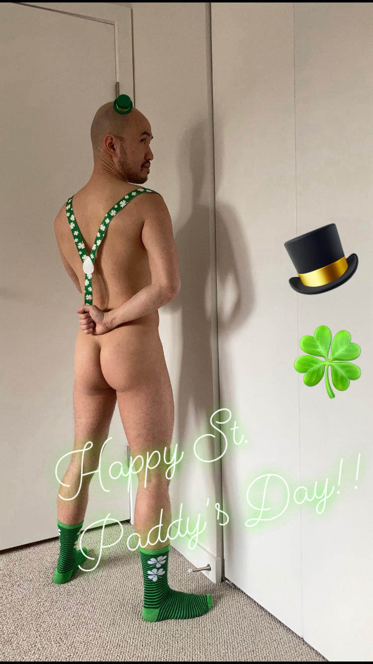 Guy facing a corner with green socks, green suspenders, and a green fascinator/hat.