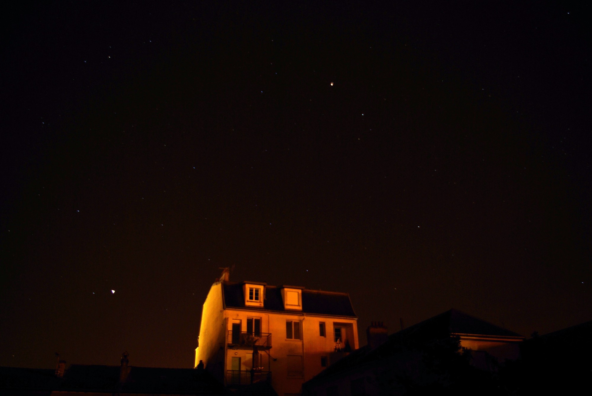 Un ciel de nuit en pleine ville.
On voit quelques étoiles. 
On voit surtout l'immeuble au premier plan, éclairé par les lumières des lampadaires.