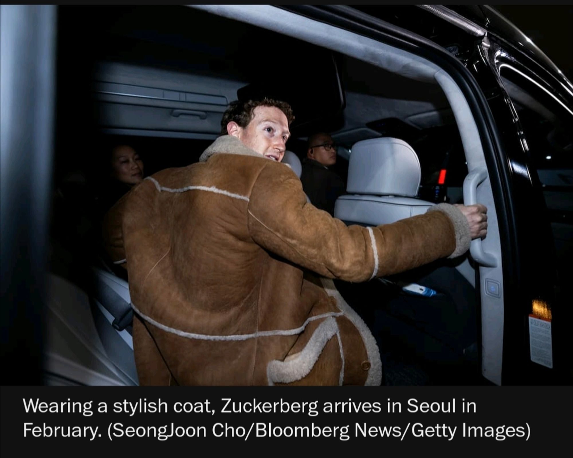 Zuckerberg photographed from the rear. He is inside an SUV, holding on to the handle near the door to help him in or out. He is wearing a bulky sheepskin coat that makes his head and hand look tiny. 'Stop Making Sense' era David Byrne would approve. The photo caption reads "Wearing a stylish coat, Zuckerberg arrives in Seoul in February."