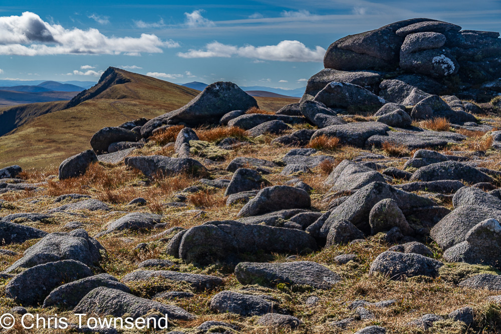 Boulders on a mountainside with a sharp pointed peak in the distance