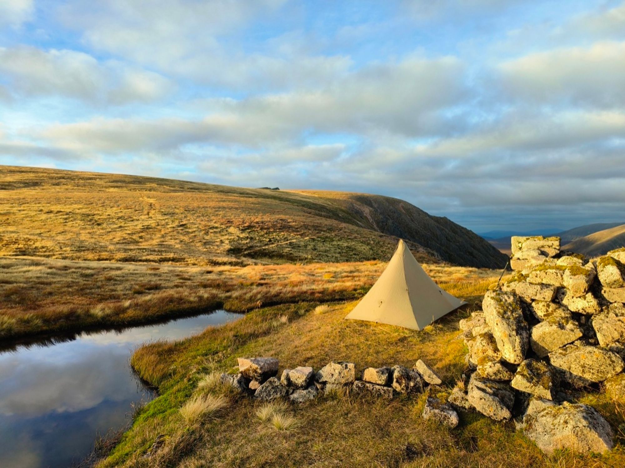 A pyramid tent by a pool in the mountains at dusk