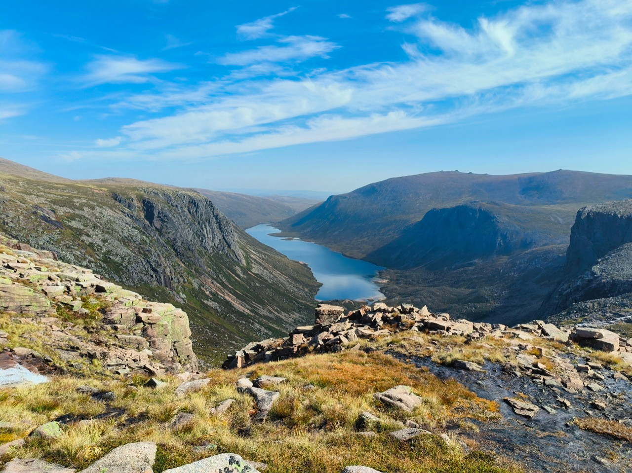 A long narrow blue mountain lake between rocky hills under a blue sky