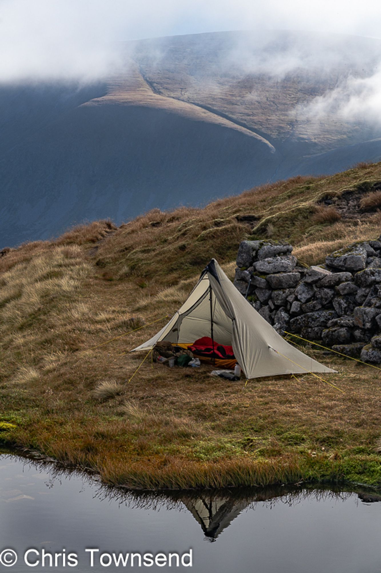 A small tent by a pool below cloud-capped hills