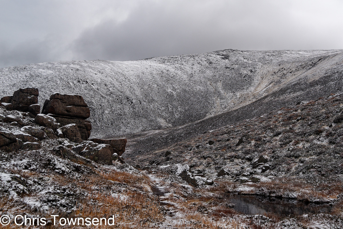 Boulders and snow in the mountains below a cloudy sky