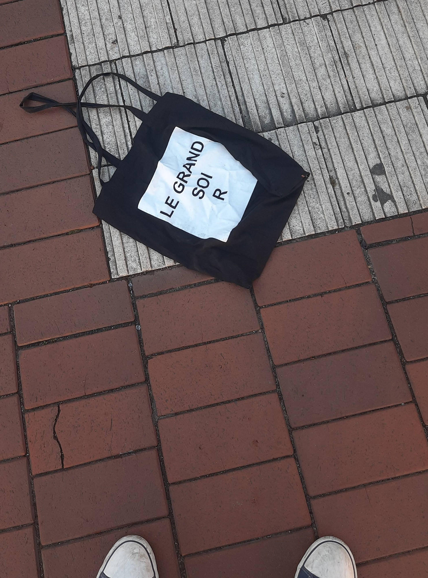 Eine Stofftasche auf Klinkerboden
Schwaz, weißes Feld Schriftzug 
LE GRAND
    SOI
      R