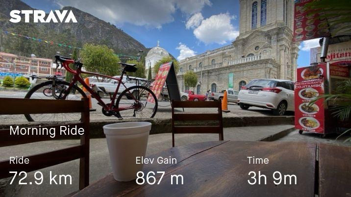 a red road bike leans against a curb. there’s a coffee in the foreground. the church of cojitambo and steep cliffs are in the background 