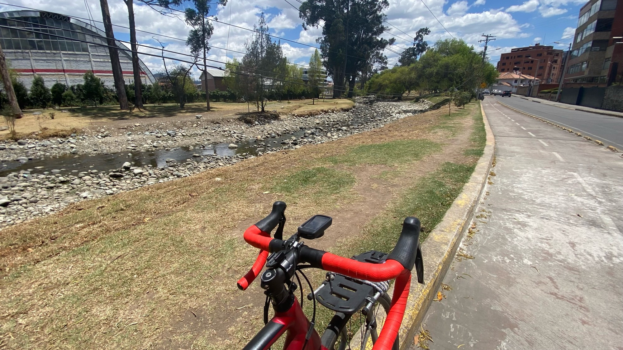 the river tomebamba with almost no water in it. the orange handlebars of a red road bike are in the foreground and there’s a bike lane that looks much better than it is