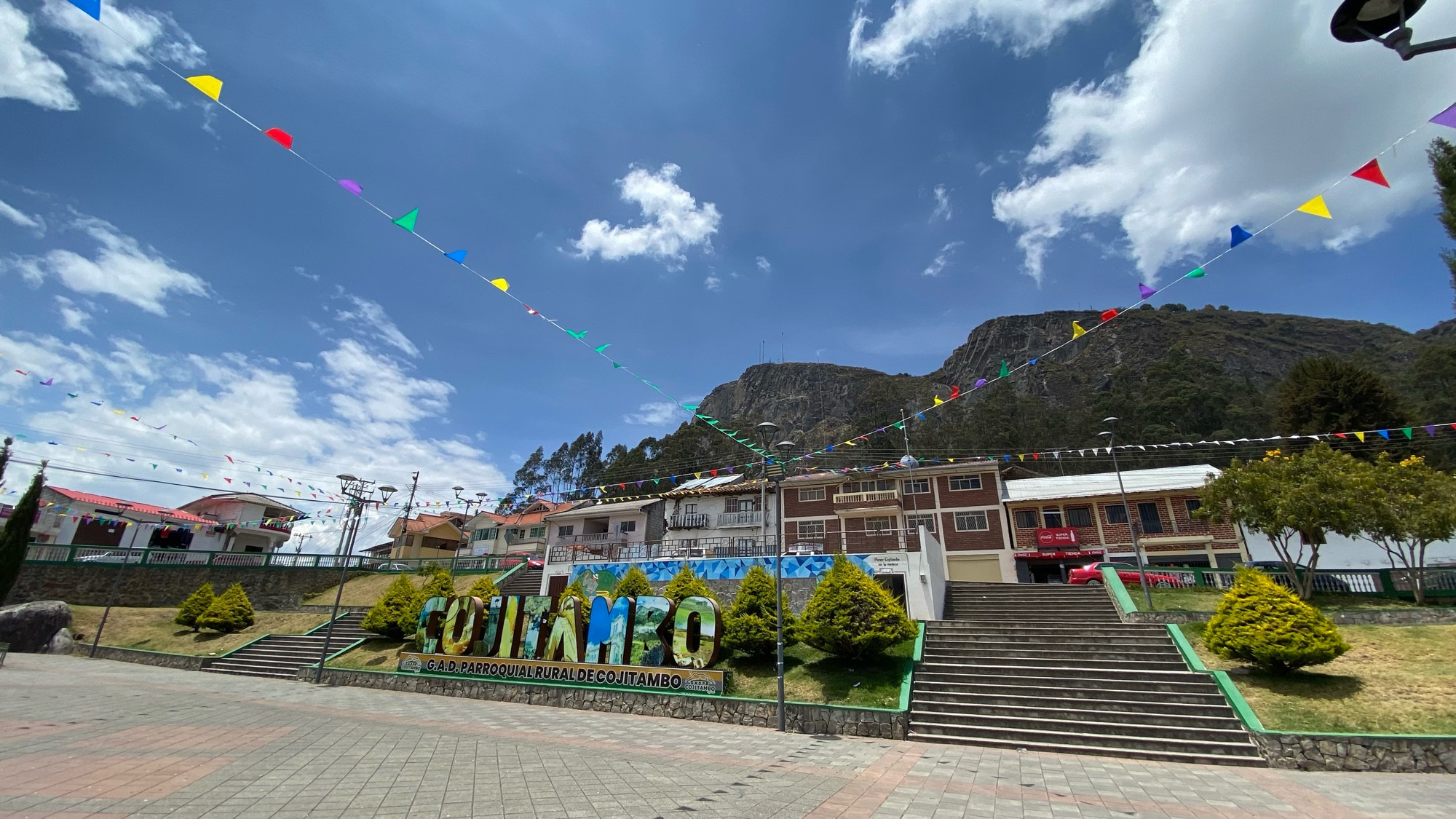 the main square of cojitambo. the name of the town is in big letters, then some shops, and behind those are huge cliffs