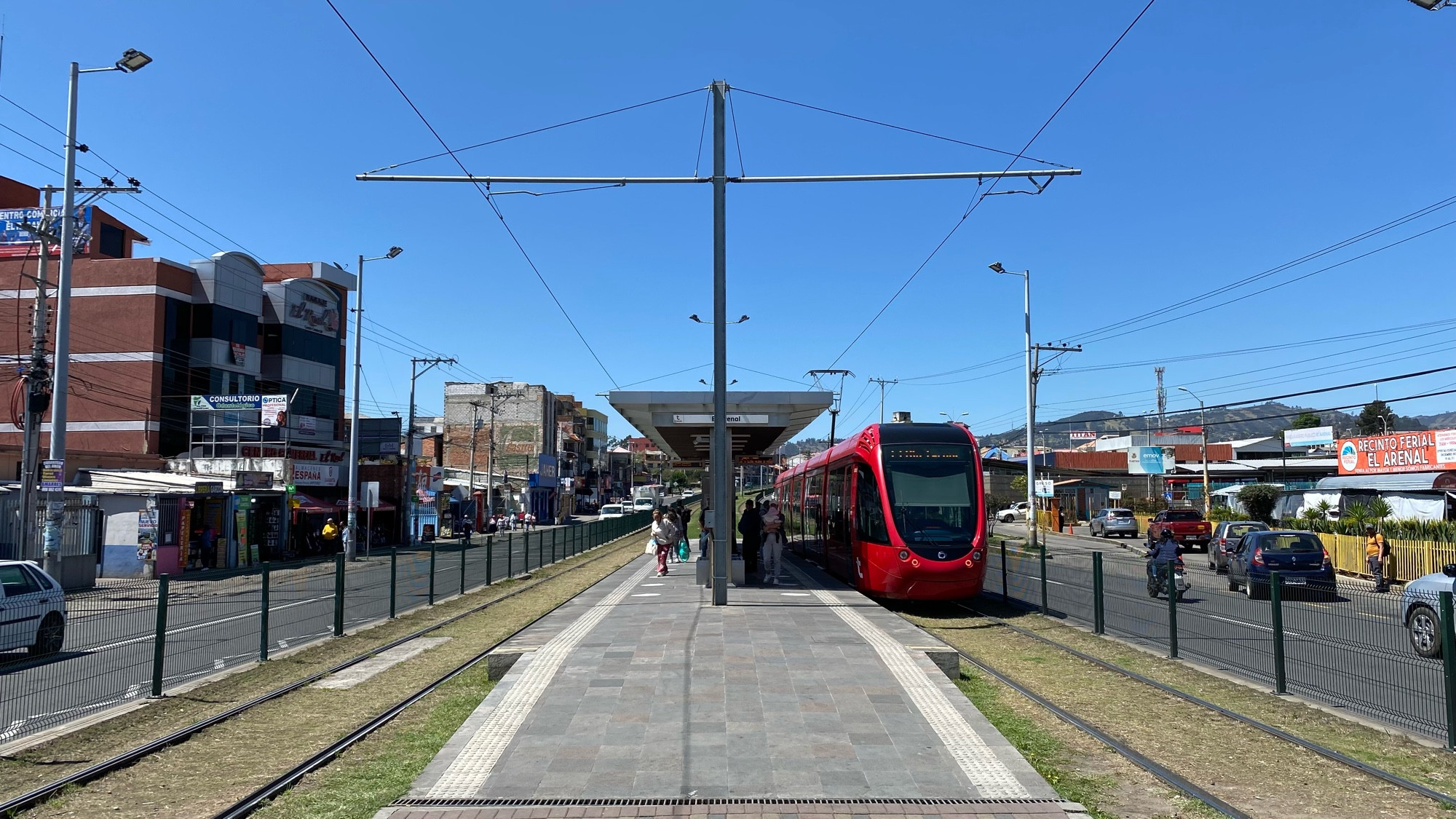 a tram stop in the middle of a dual carriageway with people boarding a pretty new red tram