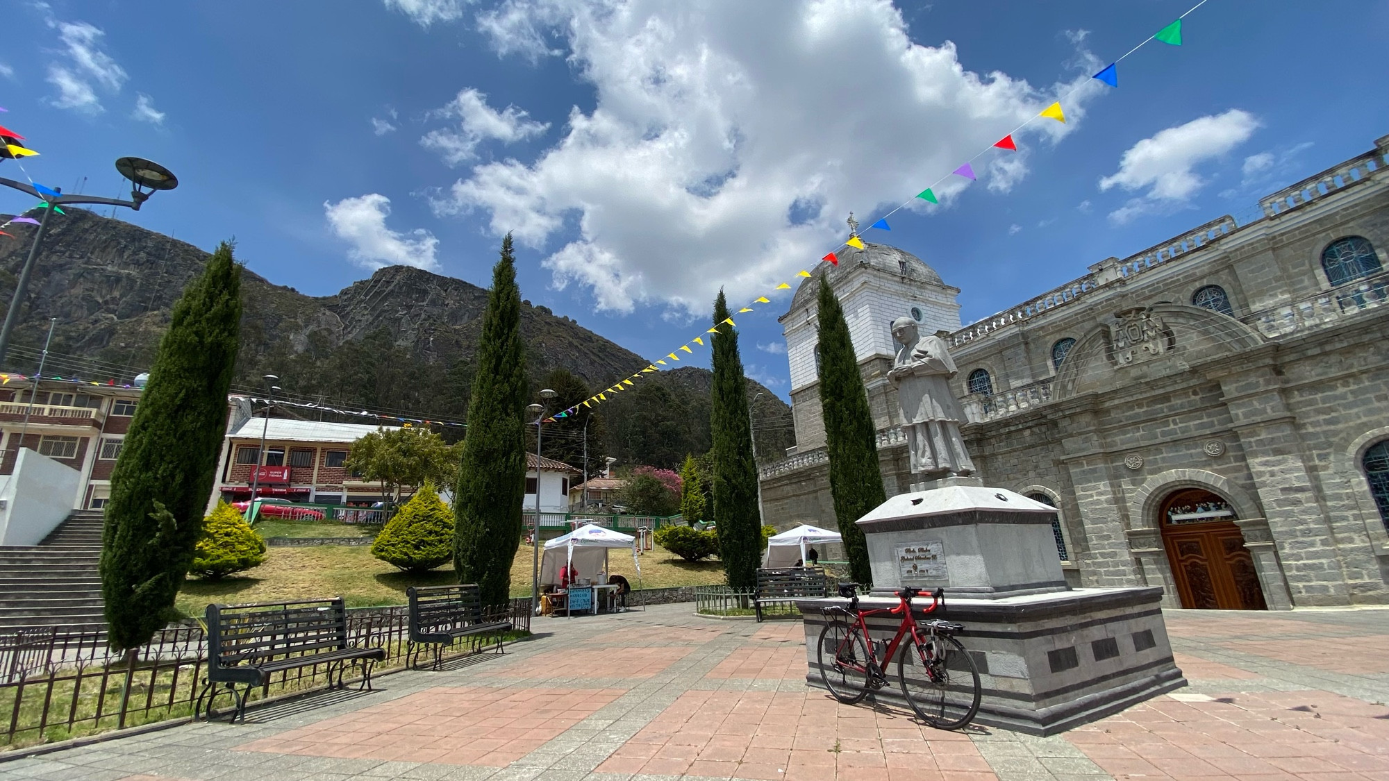 a red road bike leans against a statue of a guy who must be important to the church in cojitambo. the church is behind, as are some huge cliffs