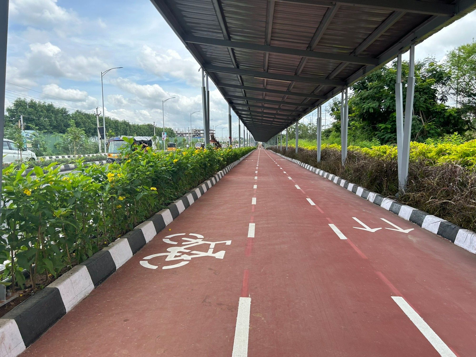 Roter überdachter Radweg, gesäumt von grünen Büschen.