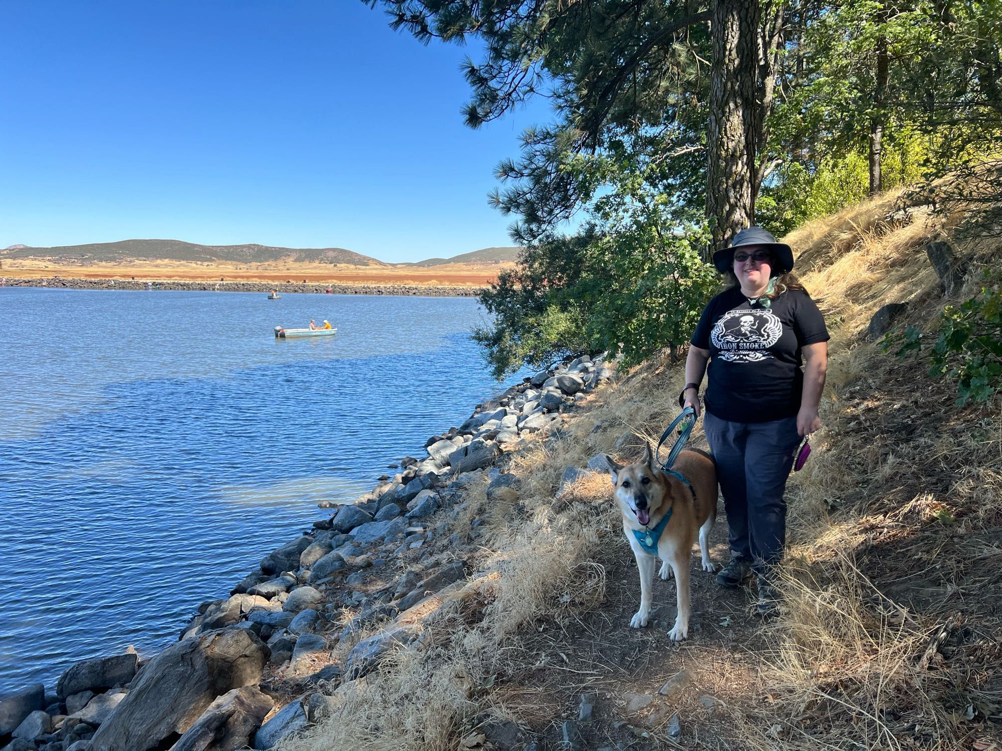 Me and my dog closer in frame looking at the camera. Lake is to the left of the shot and there is a boat on the lake with two fishermen