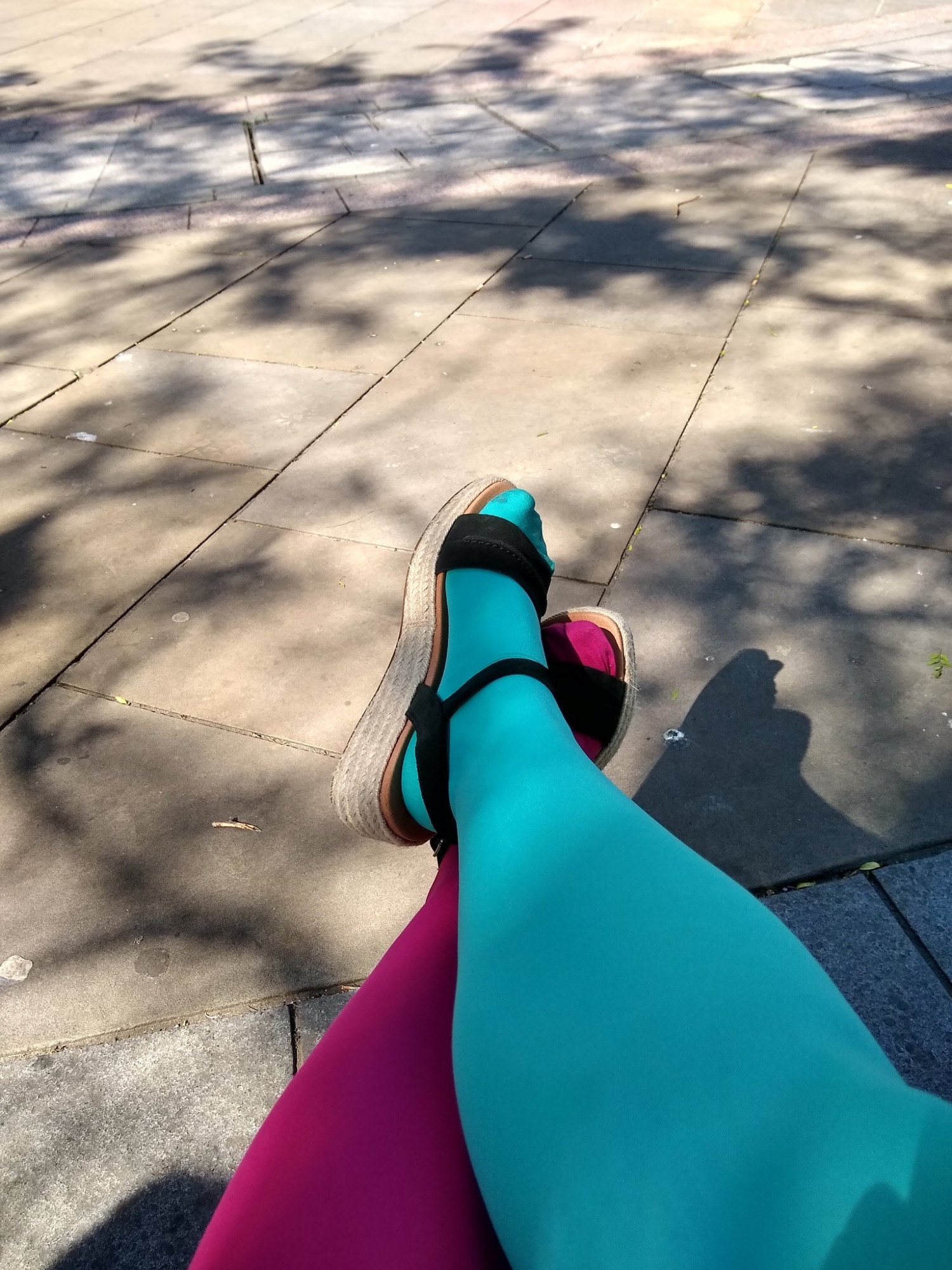 Photo of a woman's crossed legs with two-colored tights, one leg in aqua and one in hot pink.