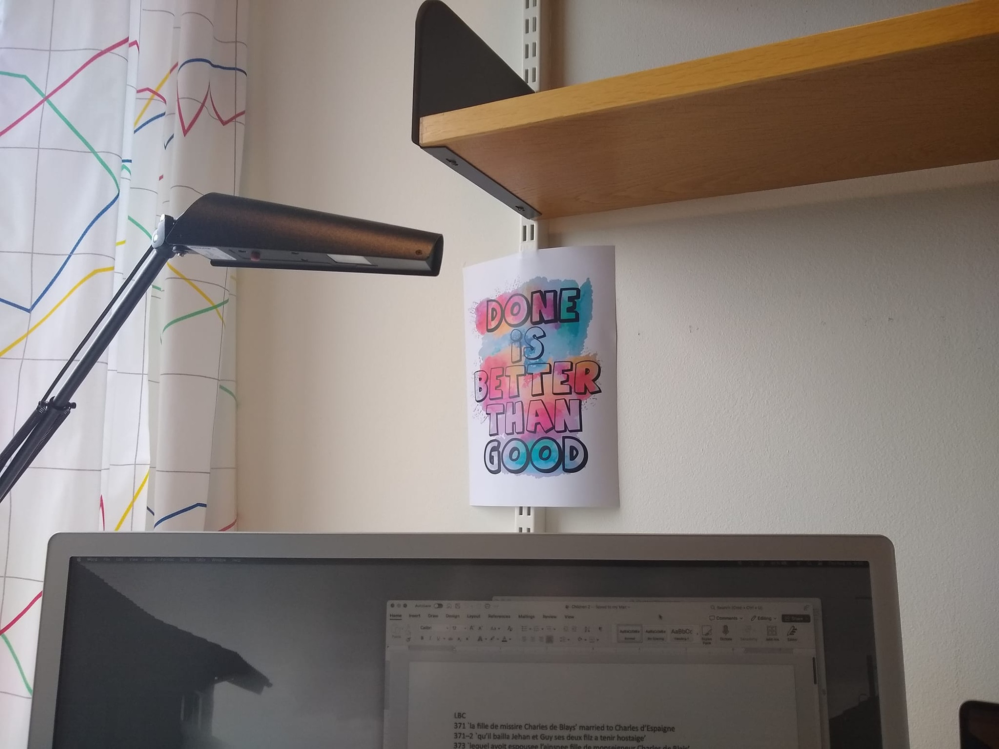 Photo of a colorful sign hung behind a computer monitor, reading DONE IS BETTER THAN GOOD