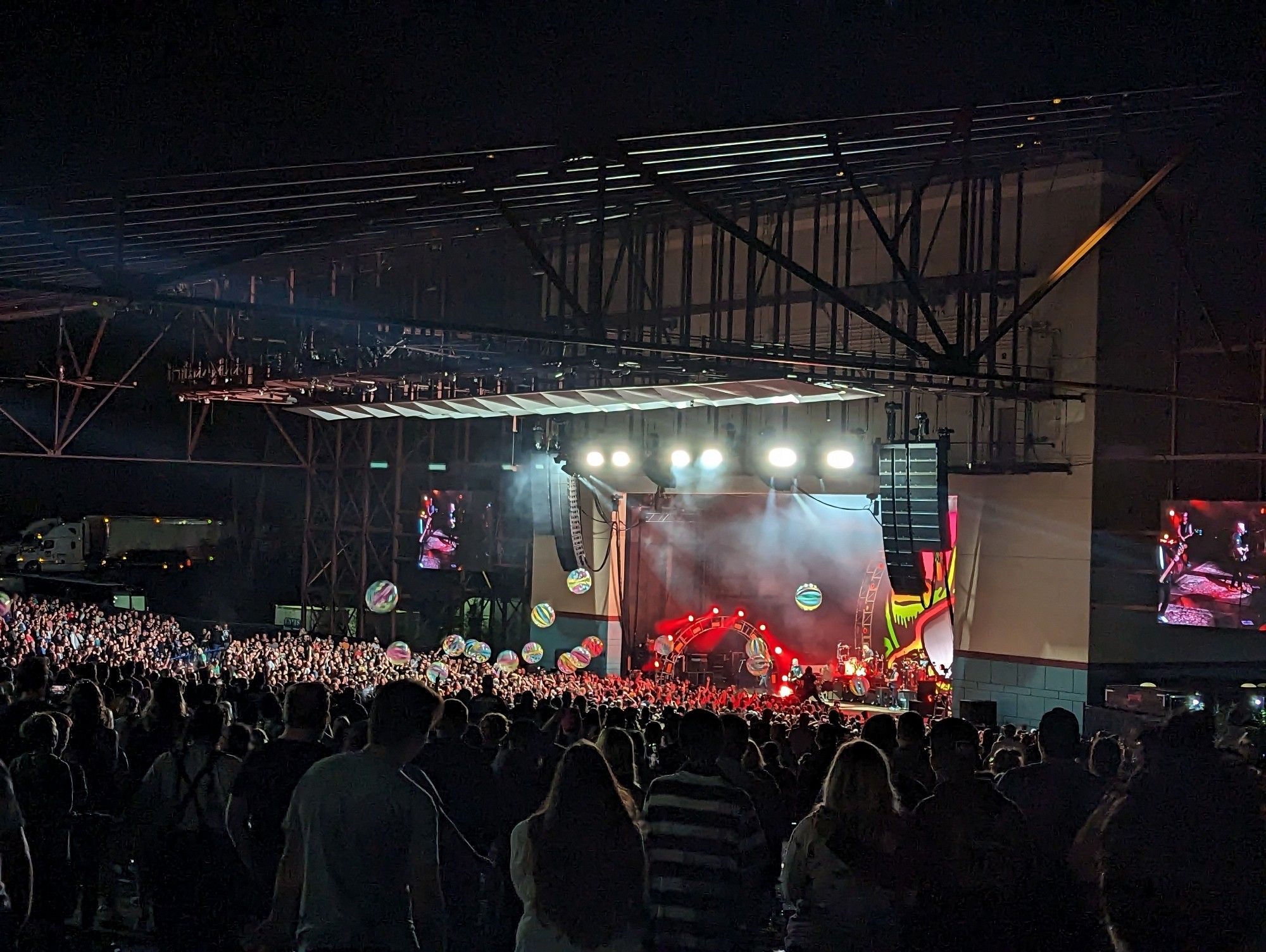 Outdoor concert venue with the pit lit up in bright lights as people hit oversized beach balls into the air. The stage is lit up mostly in red with The Offspring playing.