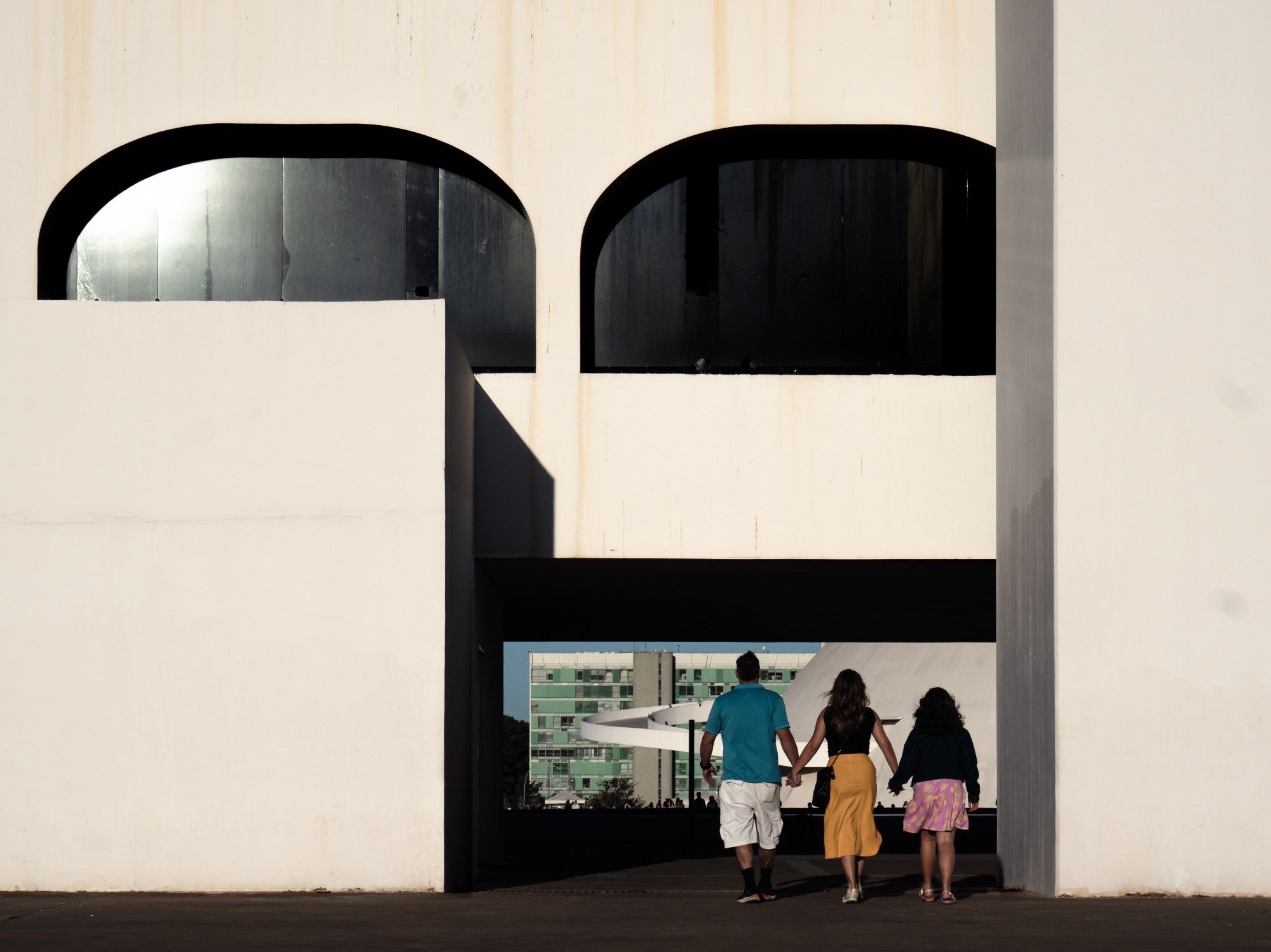 Família passa de mãos dadas por baixo do vão na Biblioteca Nacional de Brasília em direção ao Museu Nacional. Brasília, 2024.