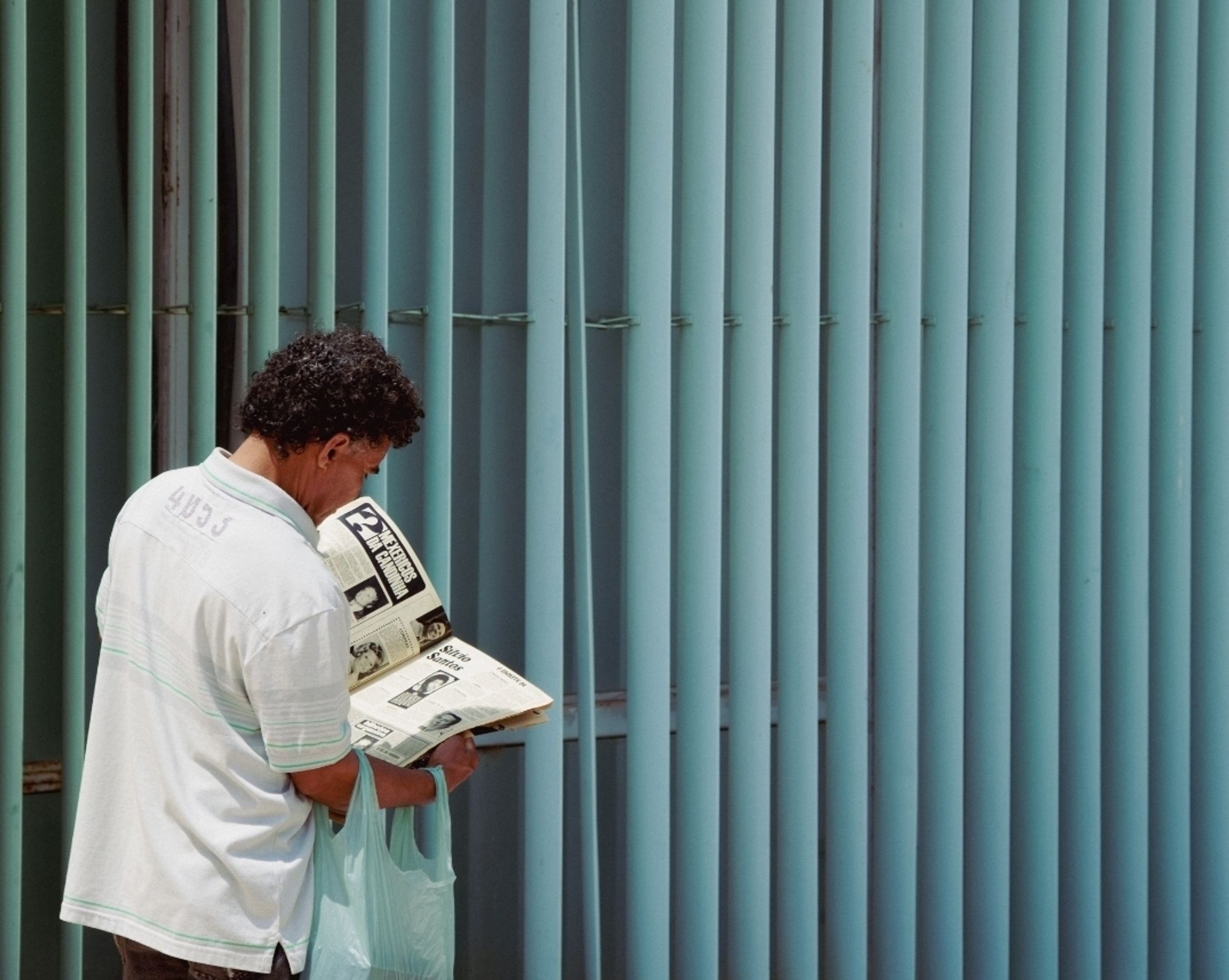 Homem lendo uma revista de costas com fundo de padrão arquitetônico de linhas verticais