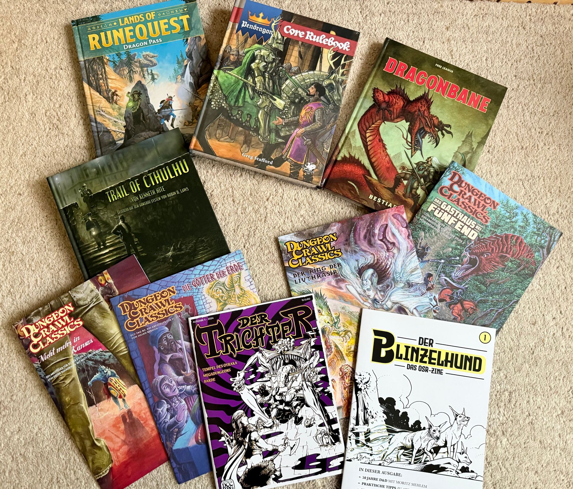 Eine Menge Rollenspielmaterial auf meinem Berberteppich ausgebreitet:
Lands of Runequest: Dragon Pass, Pendragon Core Rulebook, Dragonbane Bestiary, Trail of Cthulhu (deutsch), Der Blinzelhund (OSR-Zine von System Matters), DCC-Zine Der Trichter 5, DCC Abenteuer: Die Götter der Erde, Das Gasthaus bei Fünf End, Der Ring der Livthrasir, Nicht mehr in Kansas