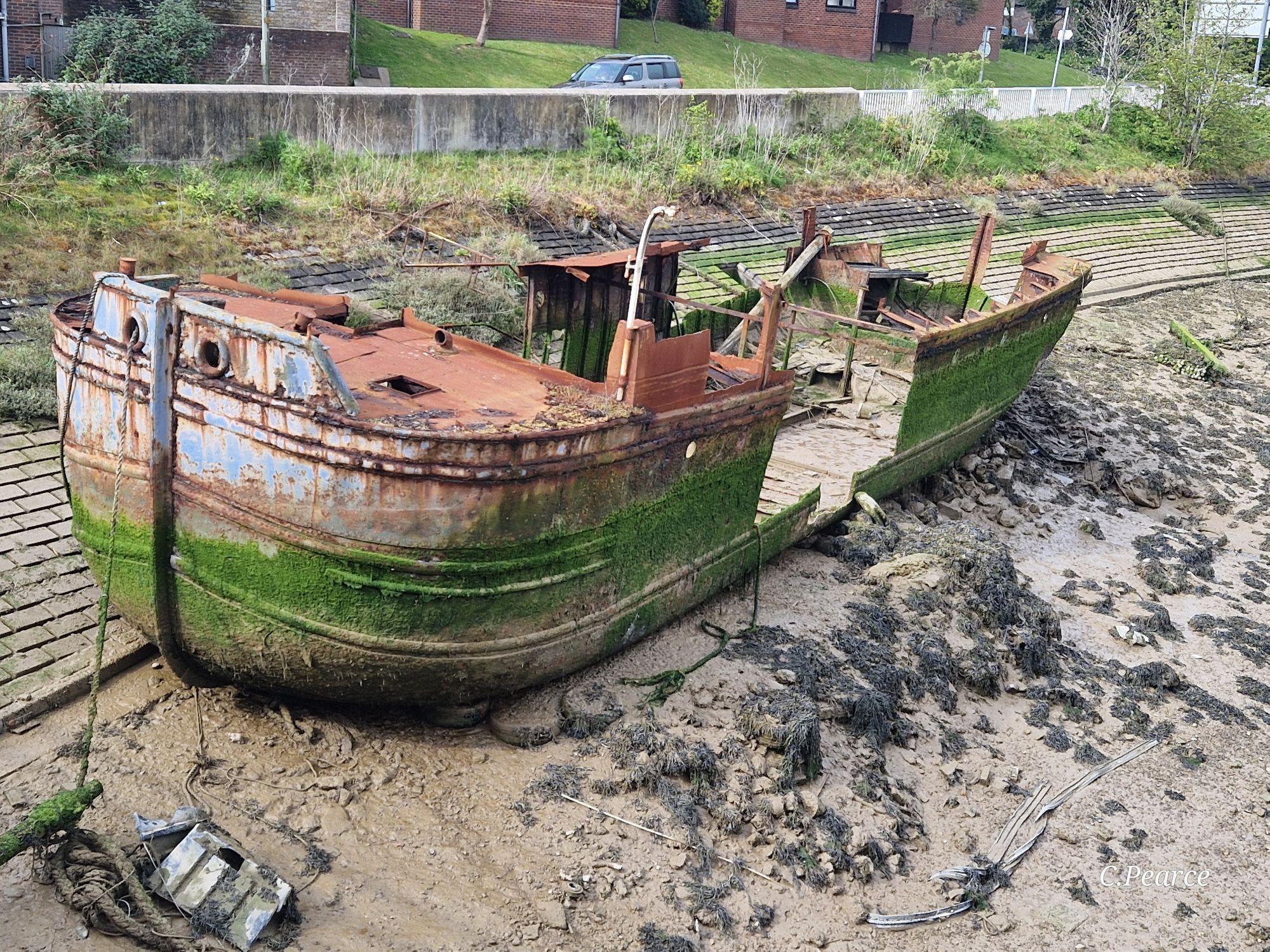 Photo of the vessel taken from the Denton Island bridge, showing it's stern. Green algae is growing halfway up the sides, showing how much is submerged during high tide.