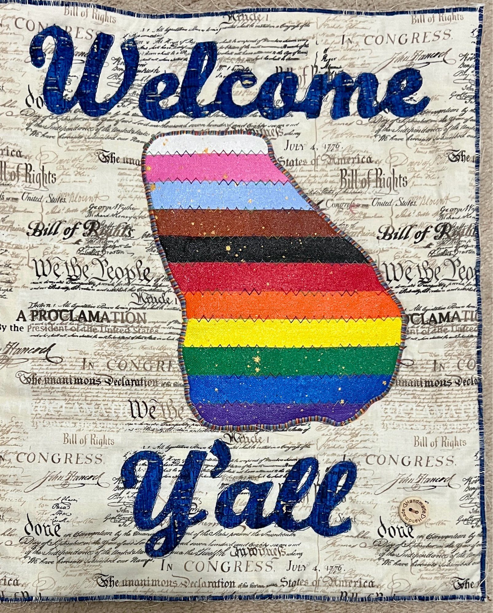 Welcome y'all text in blue with a progressive pride flag cut from acrylic canvases