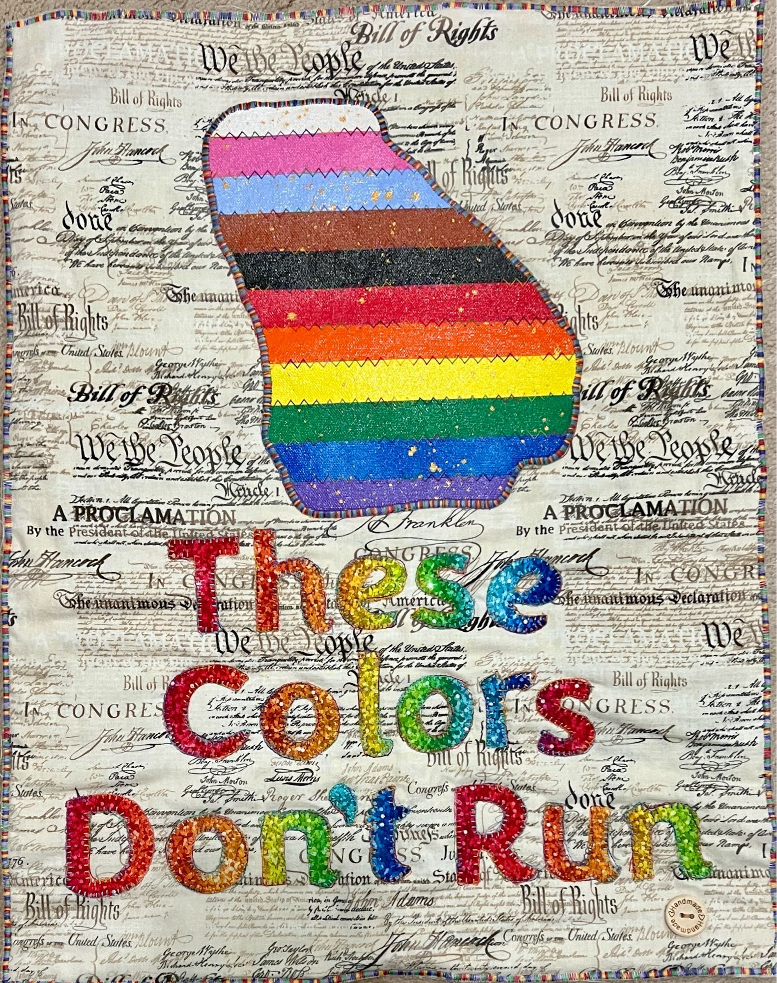 These colors don't run text in rainbow fabric with a progressive pride flag cut from acrylic canvases in shape of Georgia