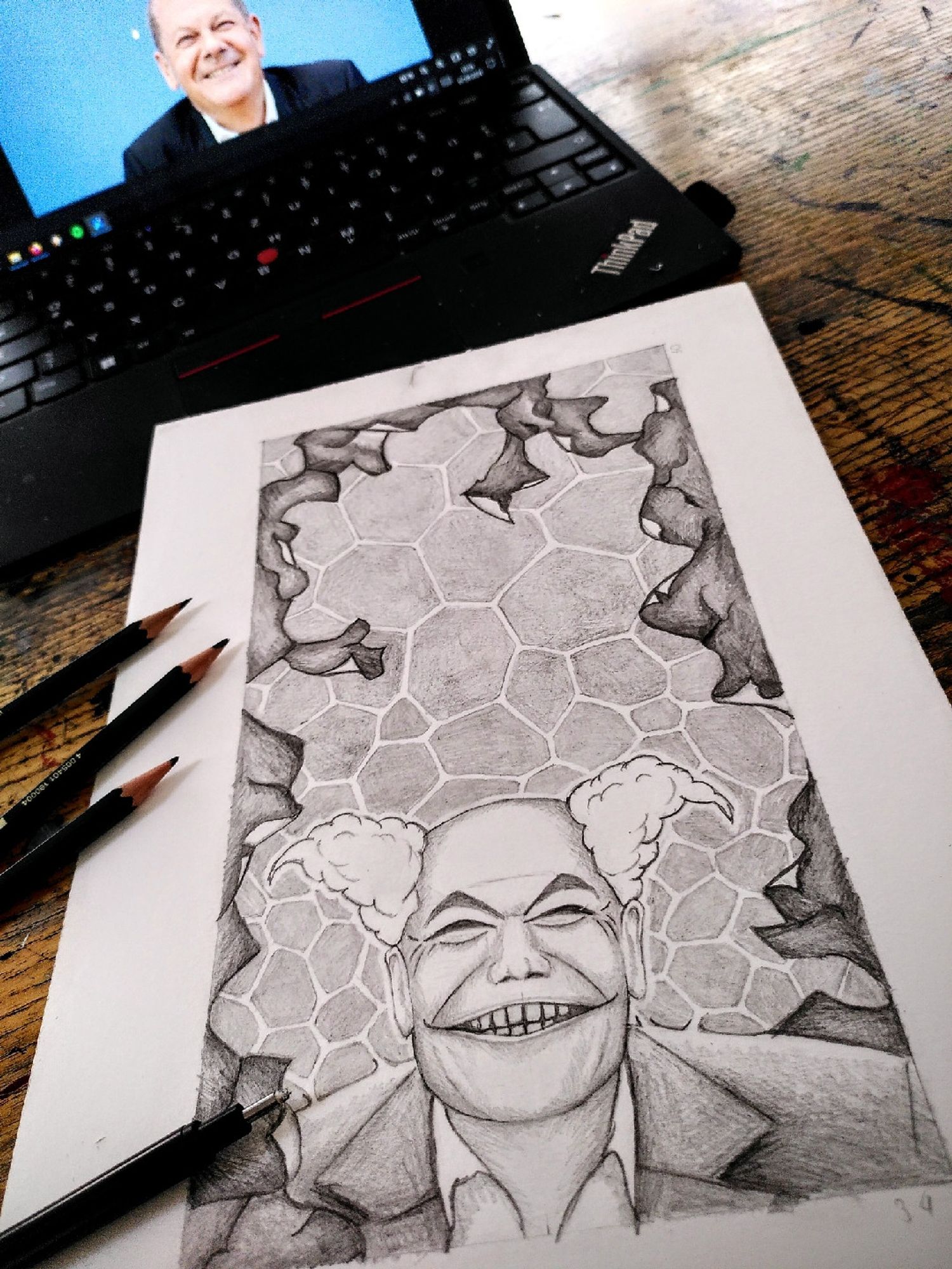 Zeichnung auf Papier mit Bleistift, schwarz-weiß, hochkant: Olaf Scholz, grinsend im Frontalprotrait, mit angedeuteten Clownsmerkmalen ( lockige Haare und geschminkt). Das Grinsen ist leicht verzerrt. Um ihn herum ist eine Struktur die an bröckelnden Putz erinnert. Im Hintergrund ist eine netzartige Struktur dargestellt.
Die Zeichnung liegt vor einem Notebook in dem das Vorlage-Foto von Olaf Scholz abgebildet ist. Um die Zeichnung herum liegen ein paar Stifte.