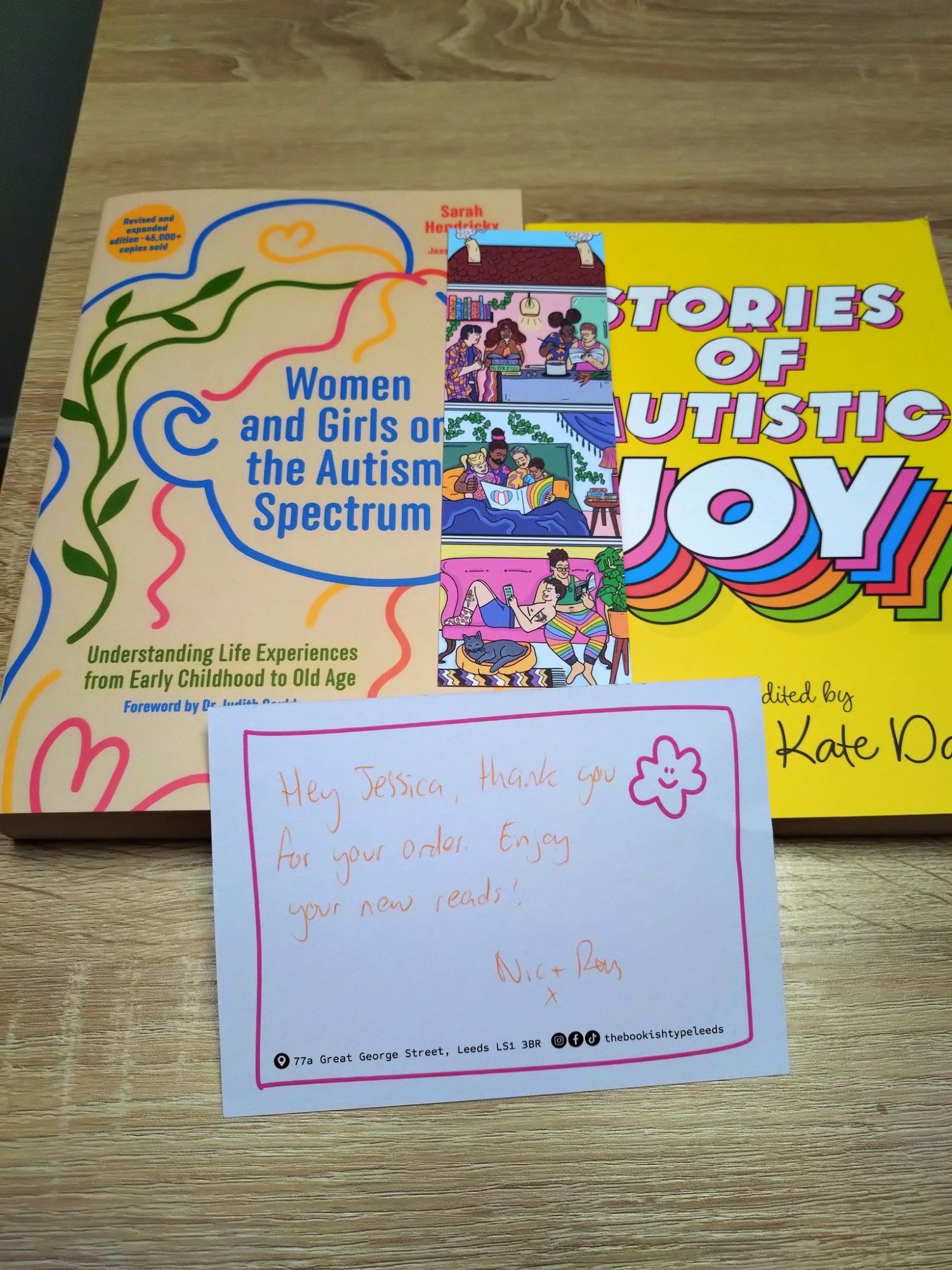 Two books - 'Women and Girls on the Autism Spectrum' by Sarah Hendrickx and 'Stories of Autistic Joy' by Laura Kate Dale. There is a handwritten note from The Bookish Type reading 'Hey Jessica thank you for your order. Enjoy your new reads - Nick + Ray' and a bookmark, which features a comic strip of people reading