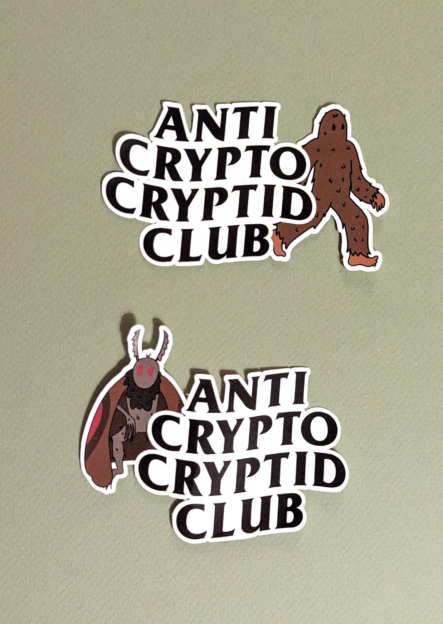 Two stickers, one each combining Bigfoot and Mothman with the "Anti Crypto Cryptid Club" design