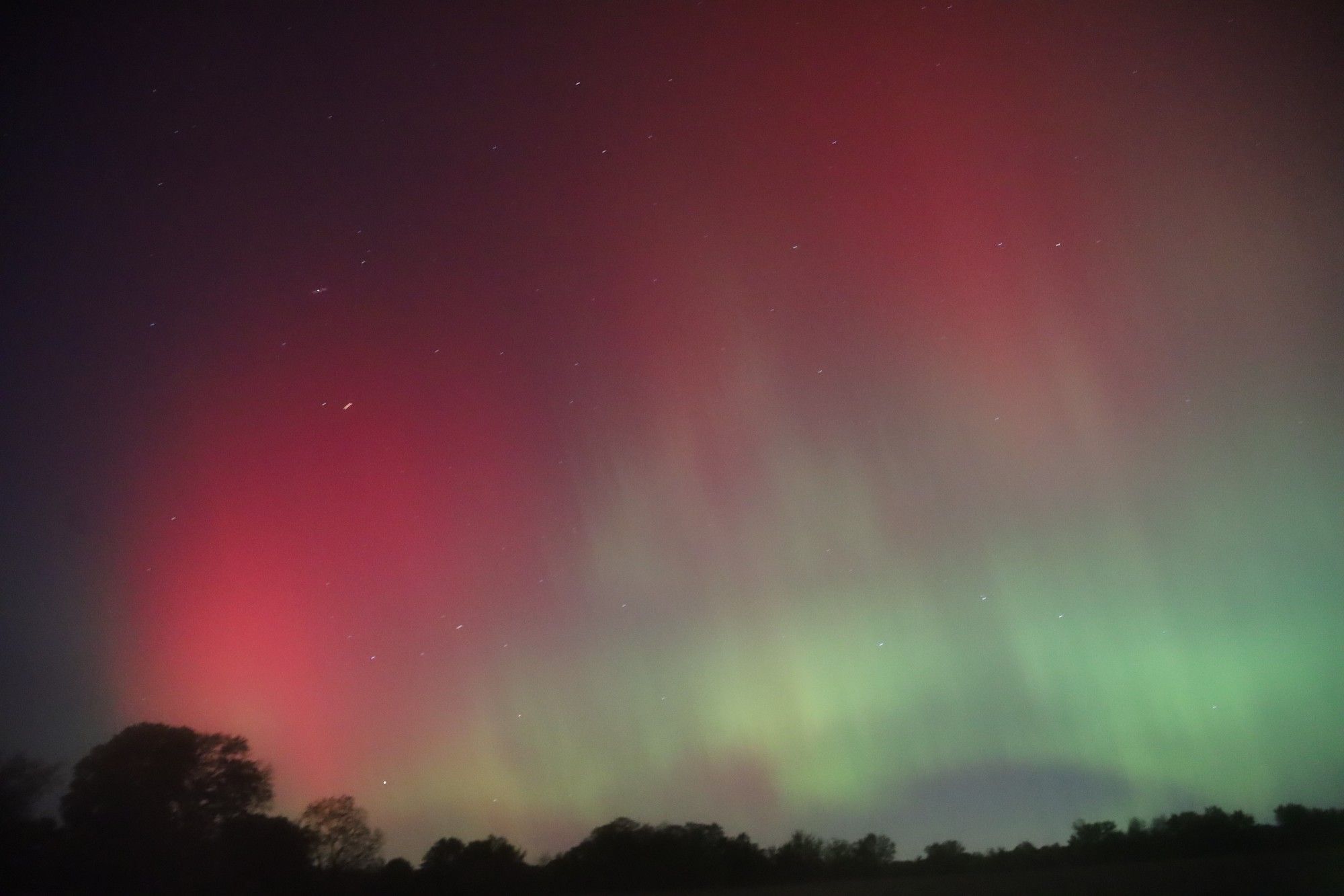 pink and yellow diffuse aurora under the milky way and above some silhouetted grass